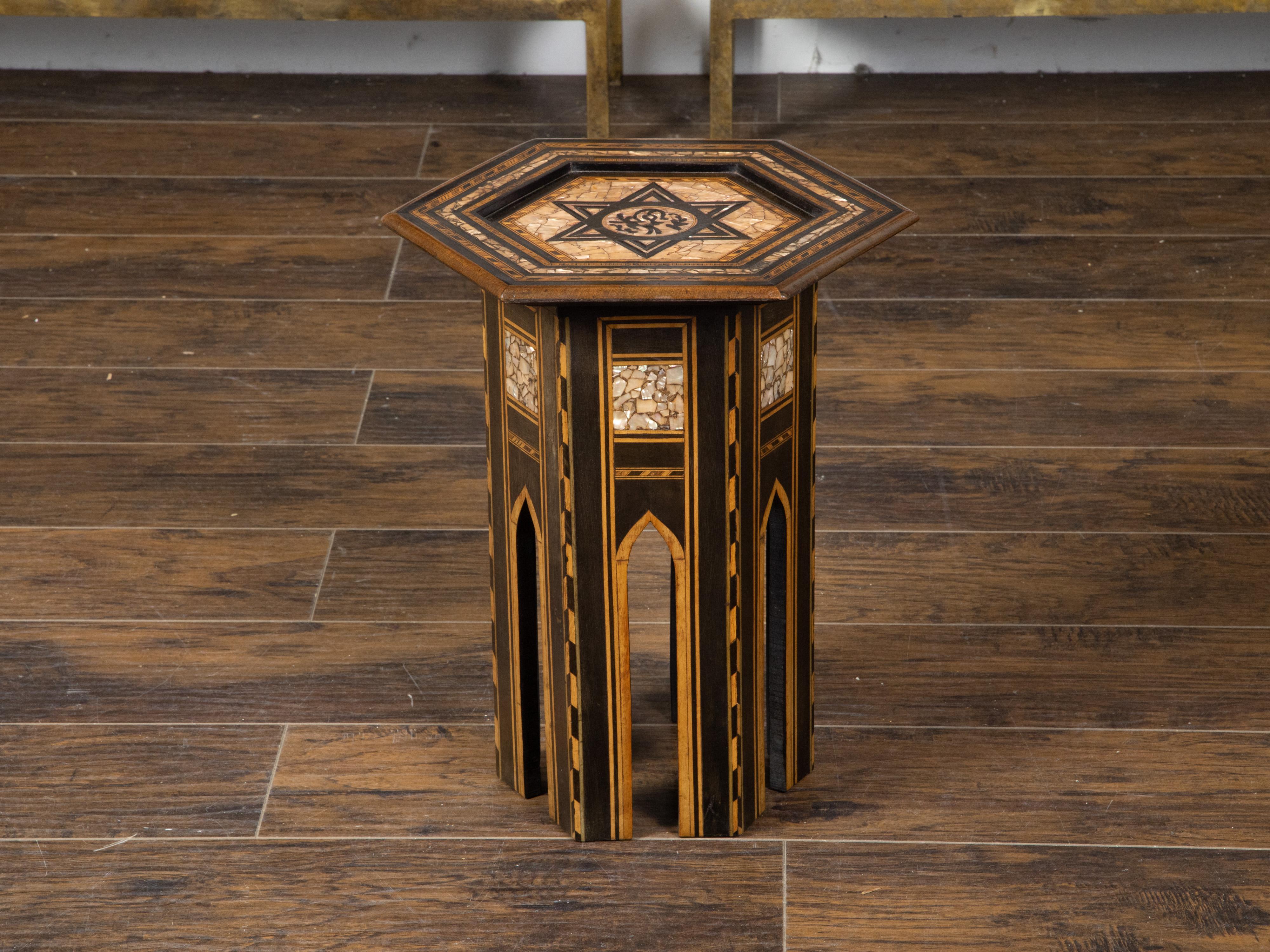 A Moroccan side table from the mid 20th century, with inlaid star motif. Created in Morocco during the midcentury period, this side table features an hexagonal top adorned with a large inlaid star surrounded by mother-of-pearl accents. Each panel of