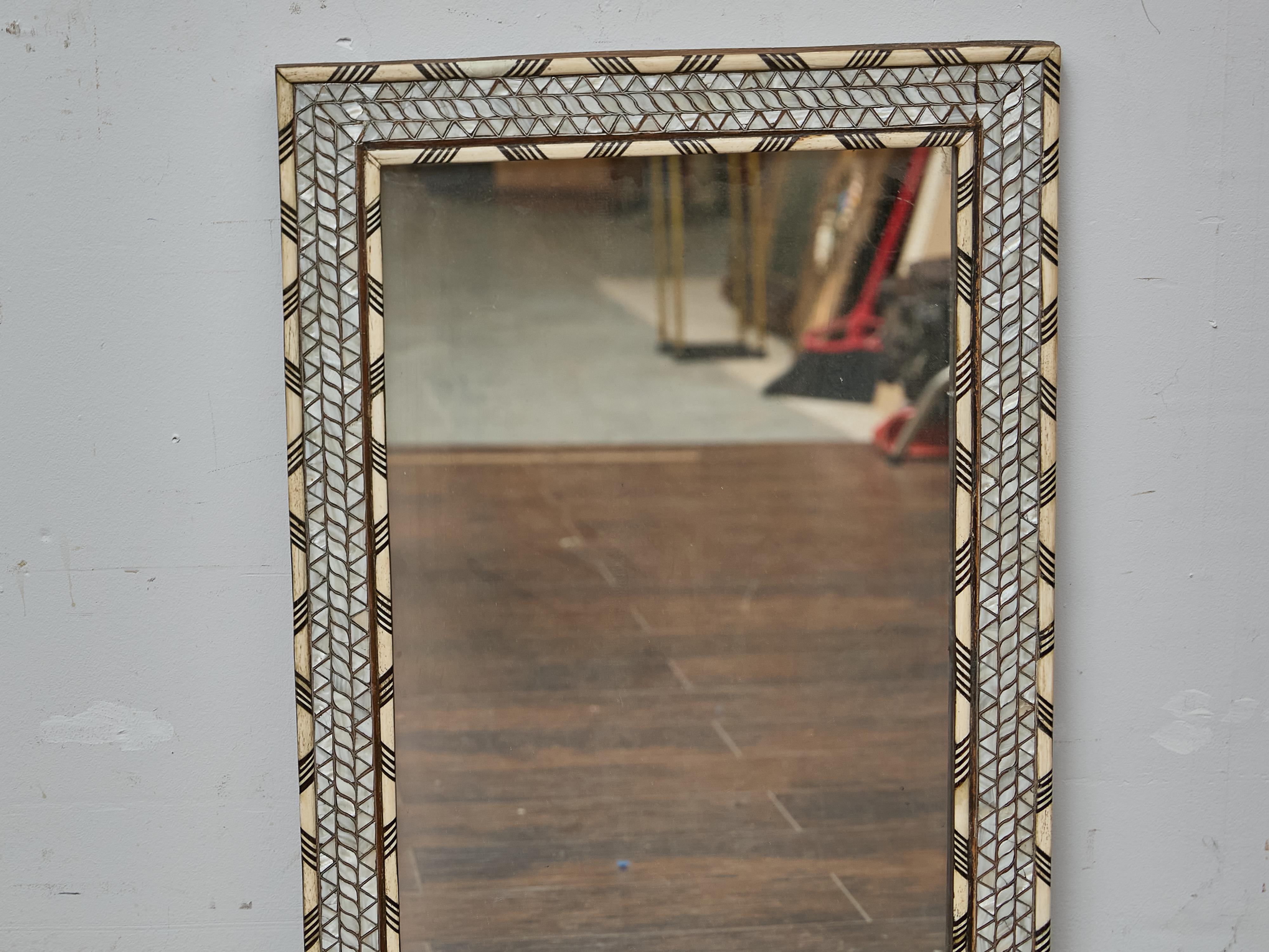 A finely detailed Moroccan mirror dating to circa 1920, featuring a striking frame adorned with inlaid bone and mother-of-pearl geometric patterns. The rectangular surround is structured in three tiers: the outer and inner bands alternate