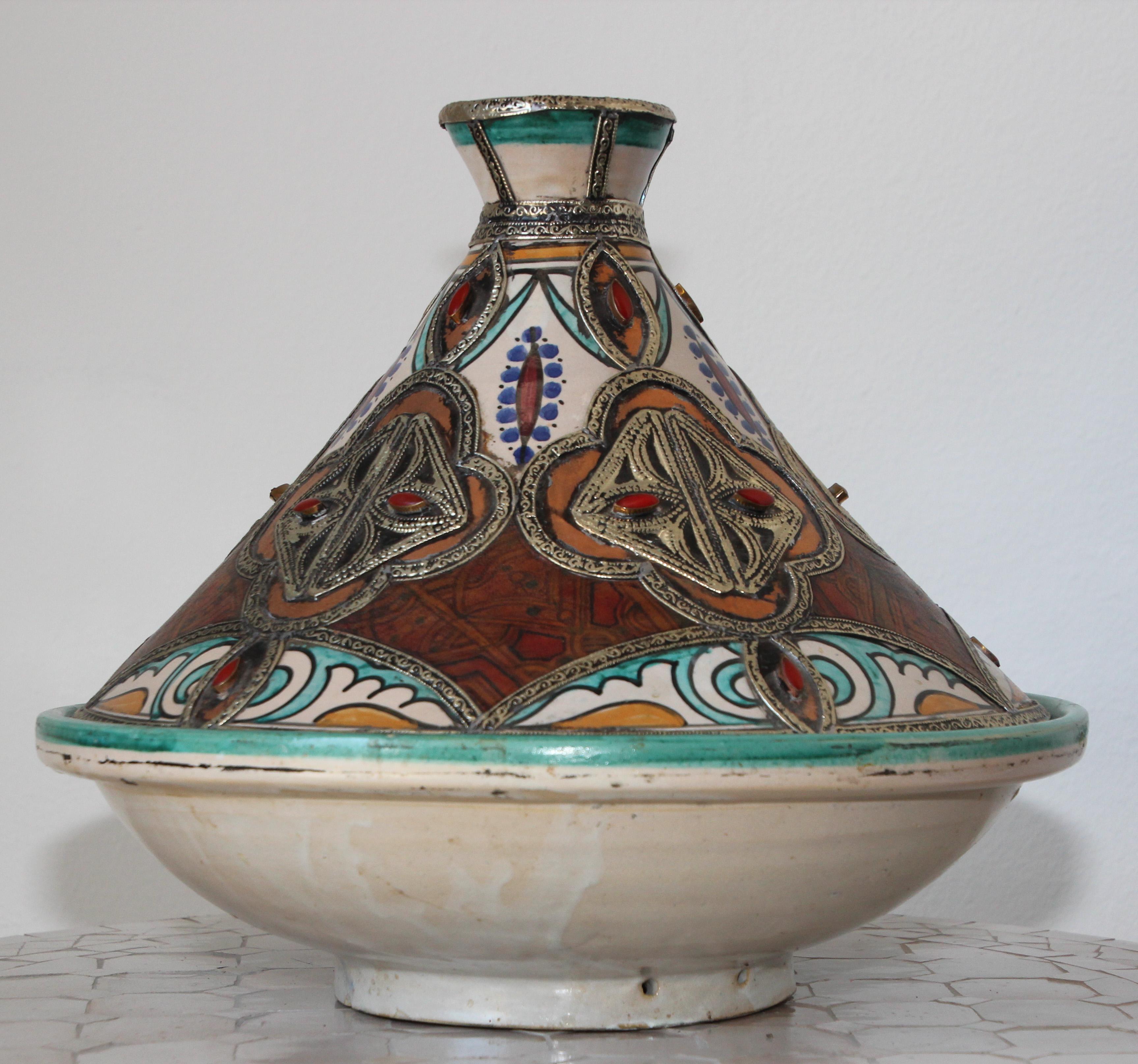 Grand tajine de service décoratif marocain en céramique polychrome avec cuir, pierres et métal, avec couvercle conique.
Le fond est un bol circulaire en céramique et le sommet du tajine a la forme d'un cône.
Fabriqués et peints à la main avec des