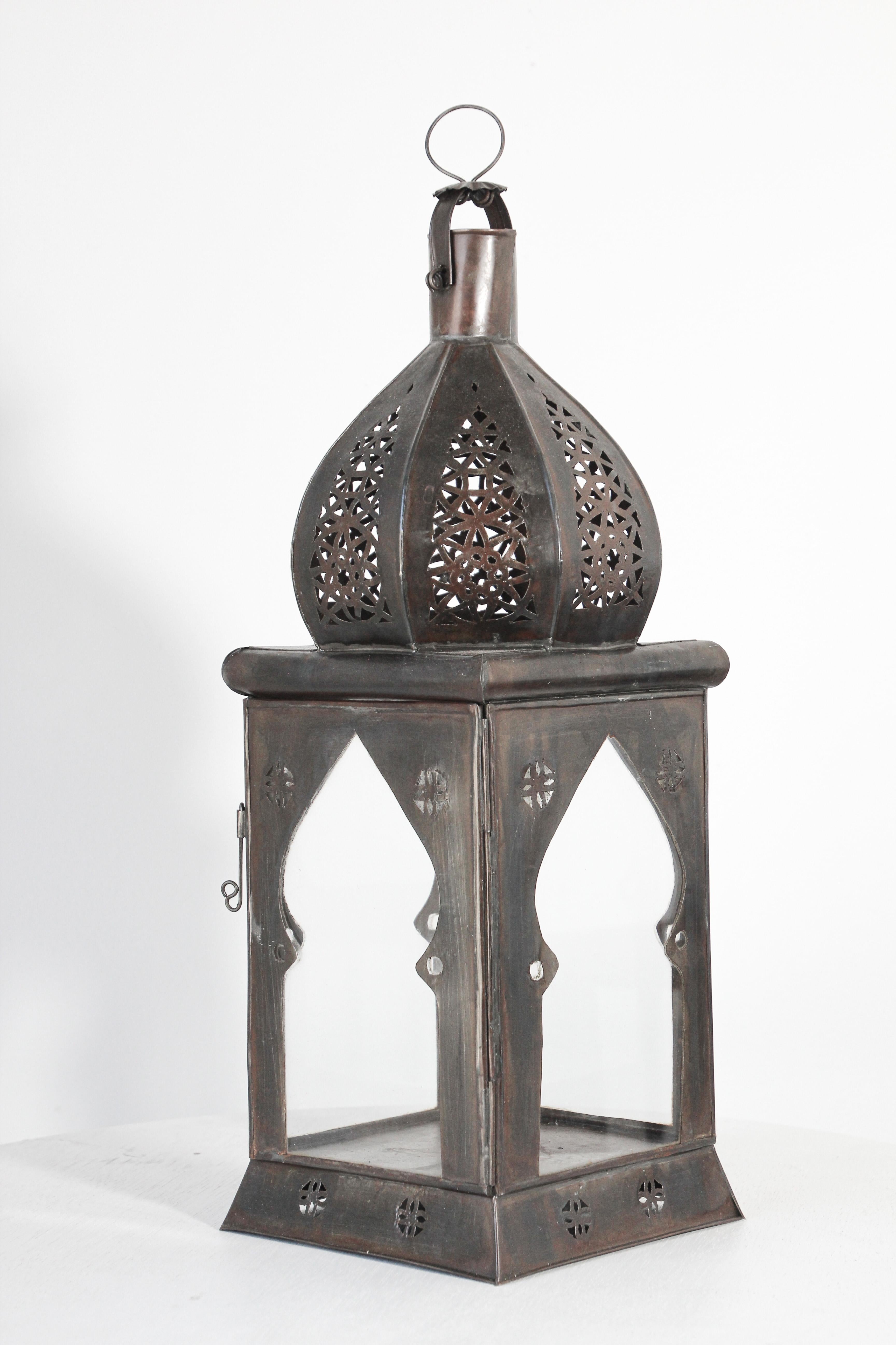 Grande lanterne marocaine en verre transparent fabriquée à la main et ornée de filigranes mauresques en métal ajouré.
Lampe à bougie de type ouragan avec un design ouvert en métal et un verre transparent.
Une petite porte permet d'accéder à