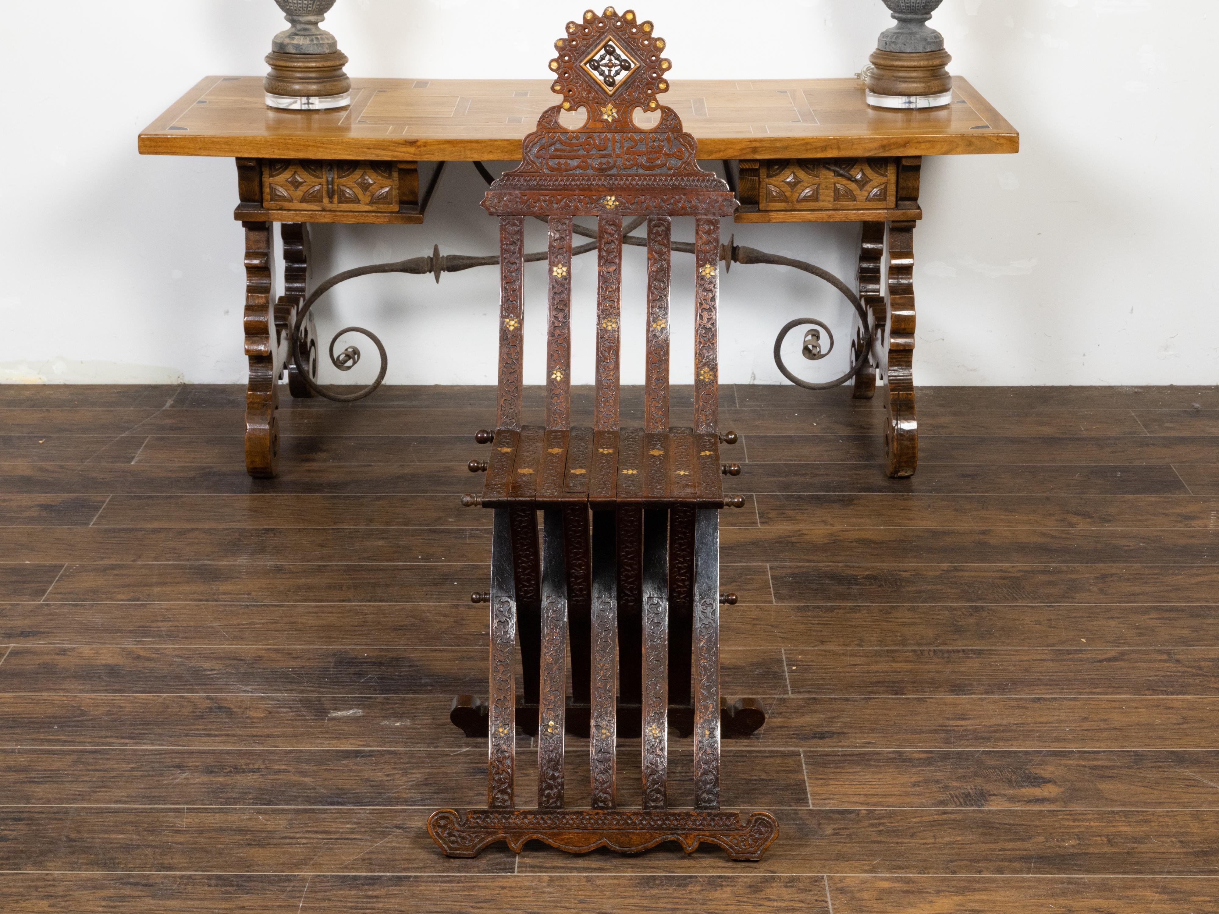 A Moroccan Moorish style accent side chair from the early 20th century, with richly carved décor, mother-of-pearl inlay, Arabic calligraphy and X-Form base. Created in Morocco during the Turn of the Century which saw the transition between the 19th