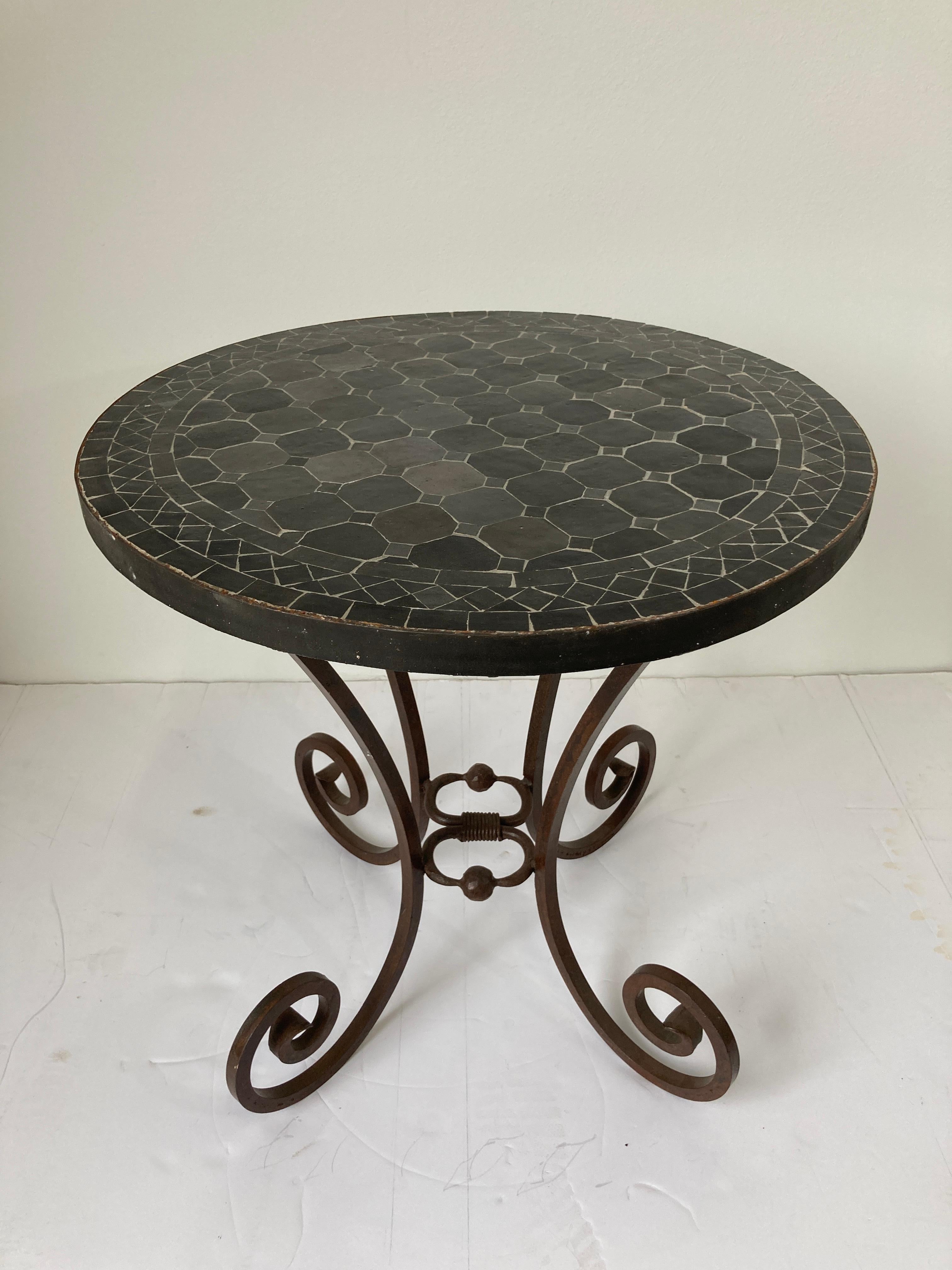 Moroccan mosaic bistro table on iron base in oxidized black tiles.
Patio tile tables handmade by expert artisans in Fez, Morocco using reclaimed old glazed black color tiles inlaid in concrete and making beautiful geometrical designs, colors are a