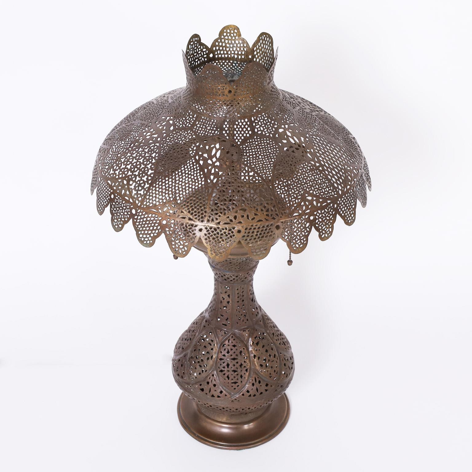 As if from the set of Casa Blanca, an alluring antique Moroccan table lamp and original matching shade hand crafted in pierced brass now having a lush bronze like patina.