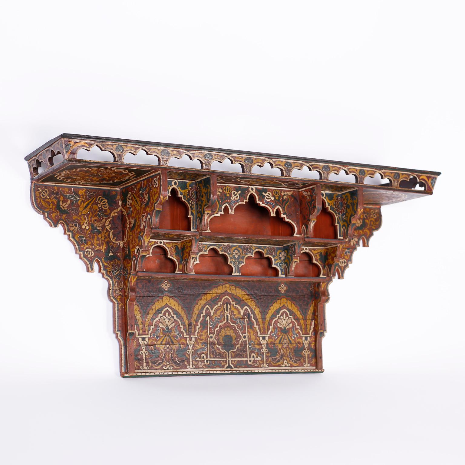 Moroccan wall shelf decorated with symbolic designs in distinctive mediterranean colors, with a gallery on top and architecturally interesting nooks.