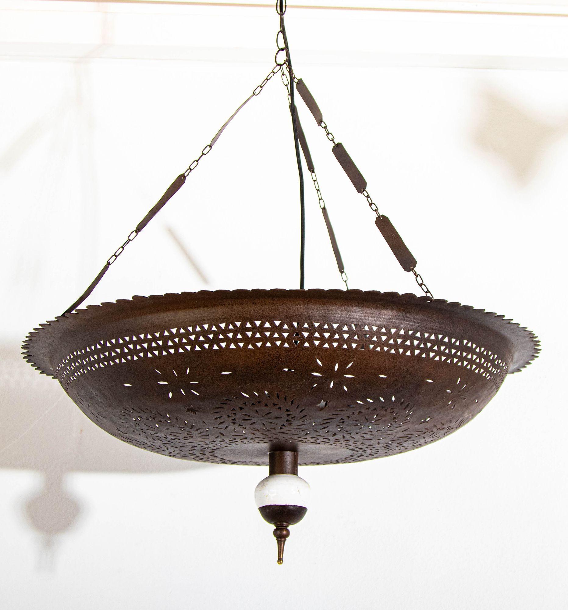 Lampadario marocchino a sospensione in metallo traforato a mano di colore bronzo patinato con terminale inferiore in ceramica bianca.
Un apparecchio a sospensione da soffitto in metallo marocchino degli anni '60 circa, ricablato con 3