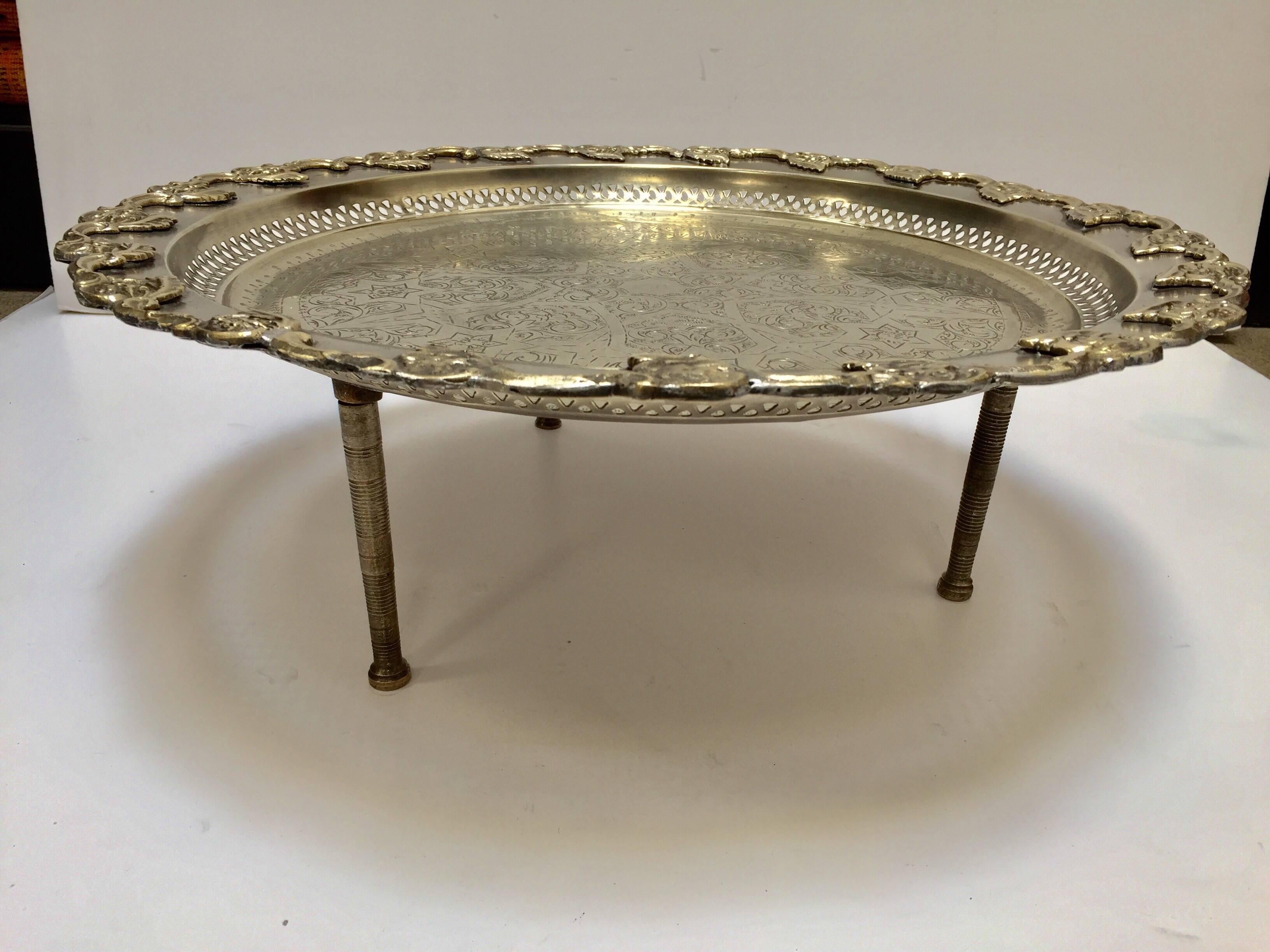 Vintage Moroccan metal silver plated polished round serving brass tray with traditional geometric designs and brass inlay decoration around on three feet.
Moroccan polished round footed silvered tray table, the feet unscrew to use as a regular