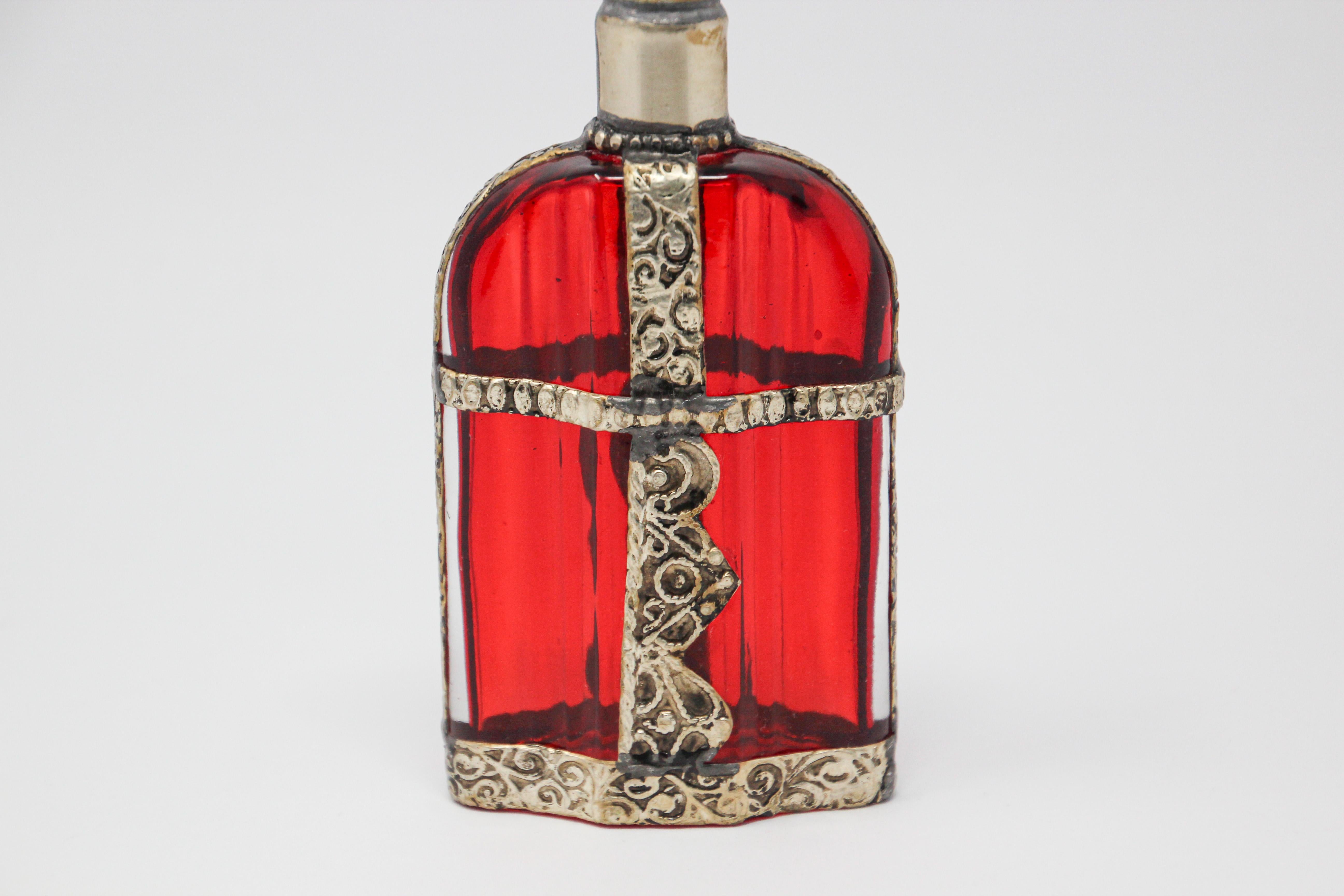 Handcrafted Moroccan Moorish red painted glass perfume bottle or rose water sprinkler with raised embossed silvered metal floral design over red glass.

The pressed glass bottle in Art Deco, Art Nouveau style is oval shape with curved sides and hand
