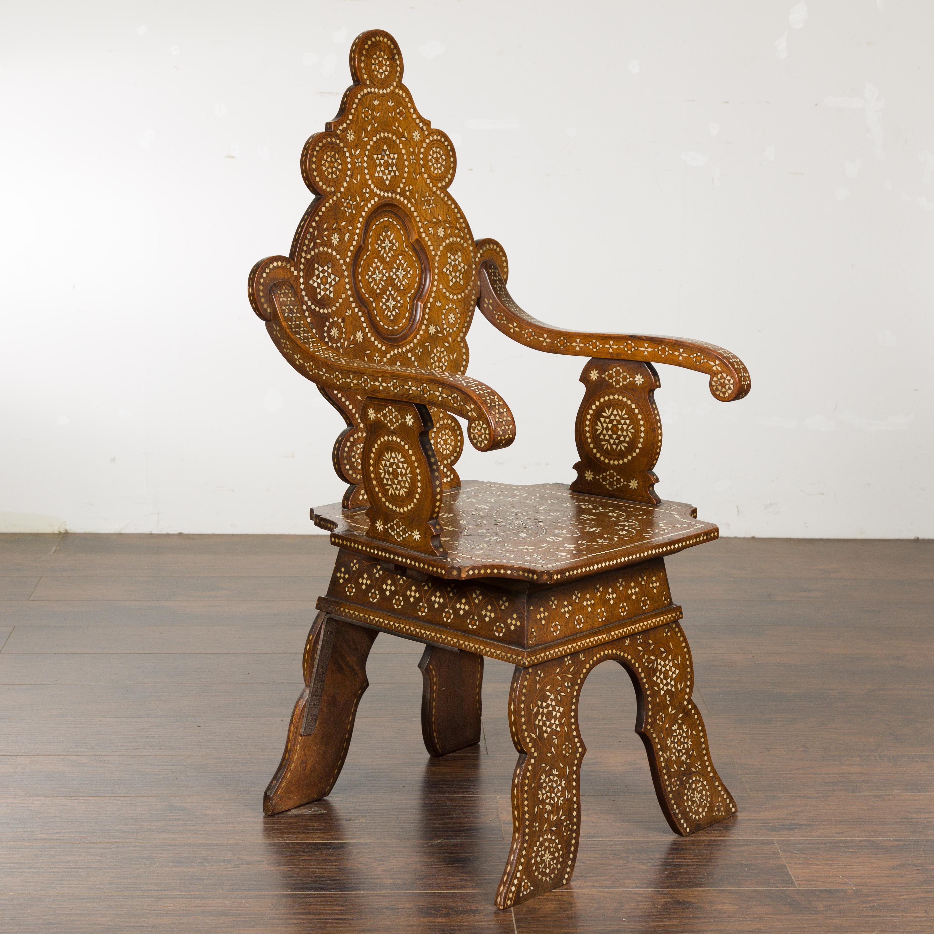 A Moorish style Moroccan wooden armchair from circa 1900 with bone inlaid décor, carved back, scrolling arms and carved base. This exquisite Moorish-style Moroccan wooden armchair, dating from circa 1900, is a stunning testament to masterful