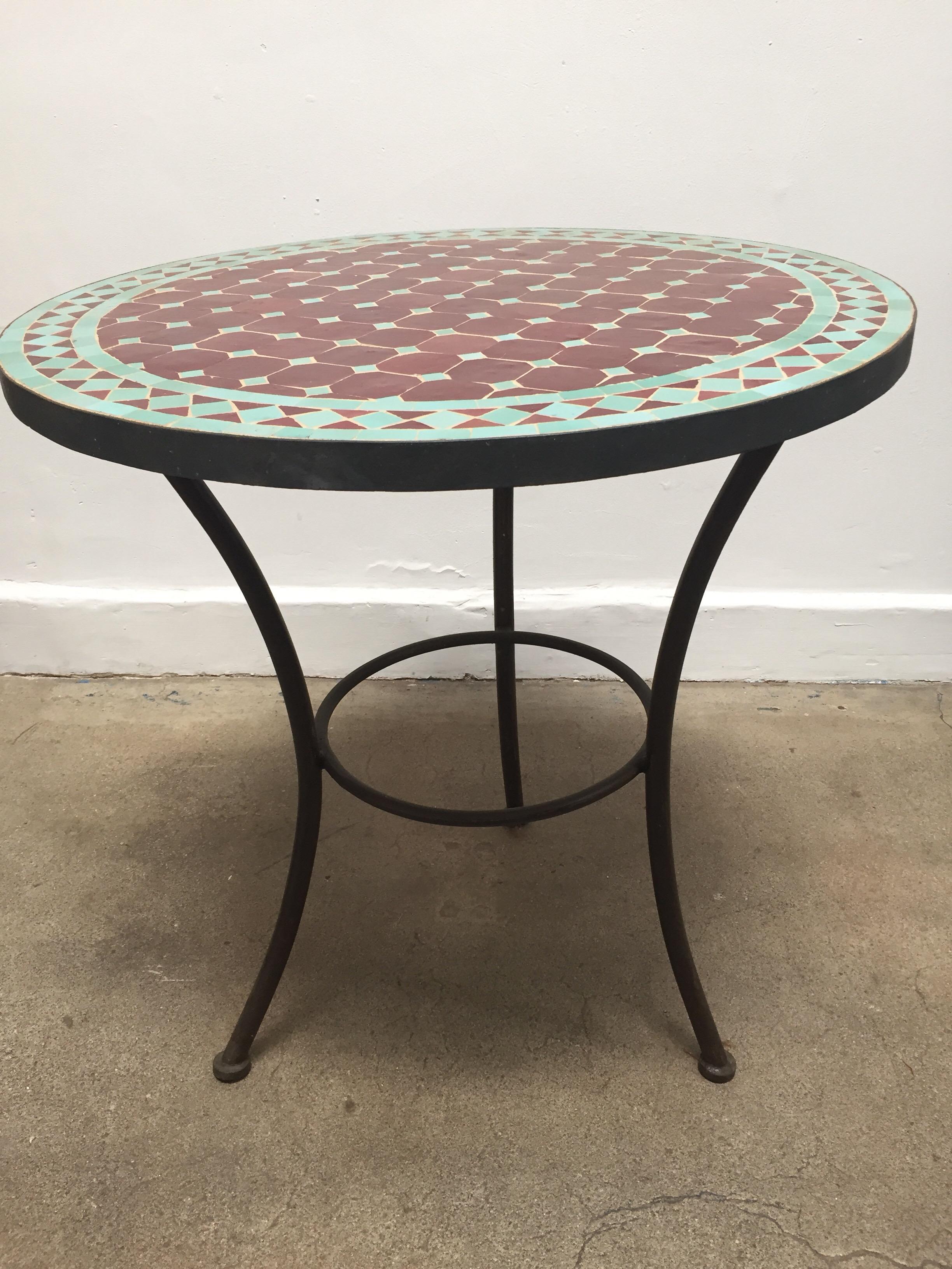 Moroccan round mosaic tile bistro table on iron base.
Green and burgundy tiles hand cut in geometrical designs.
Hand-made by expert artisans in Fez using reclaimed old glazed tiles and making beautiful geometrical designs, colors are aqua green