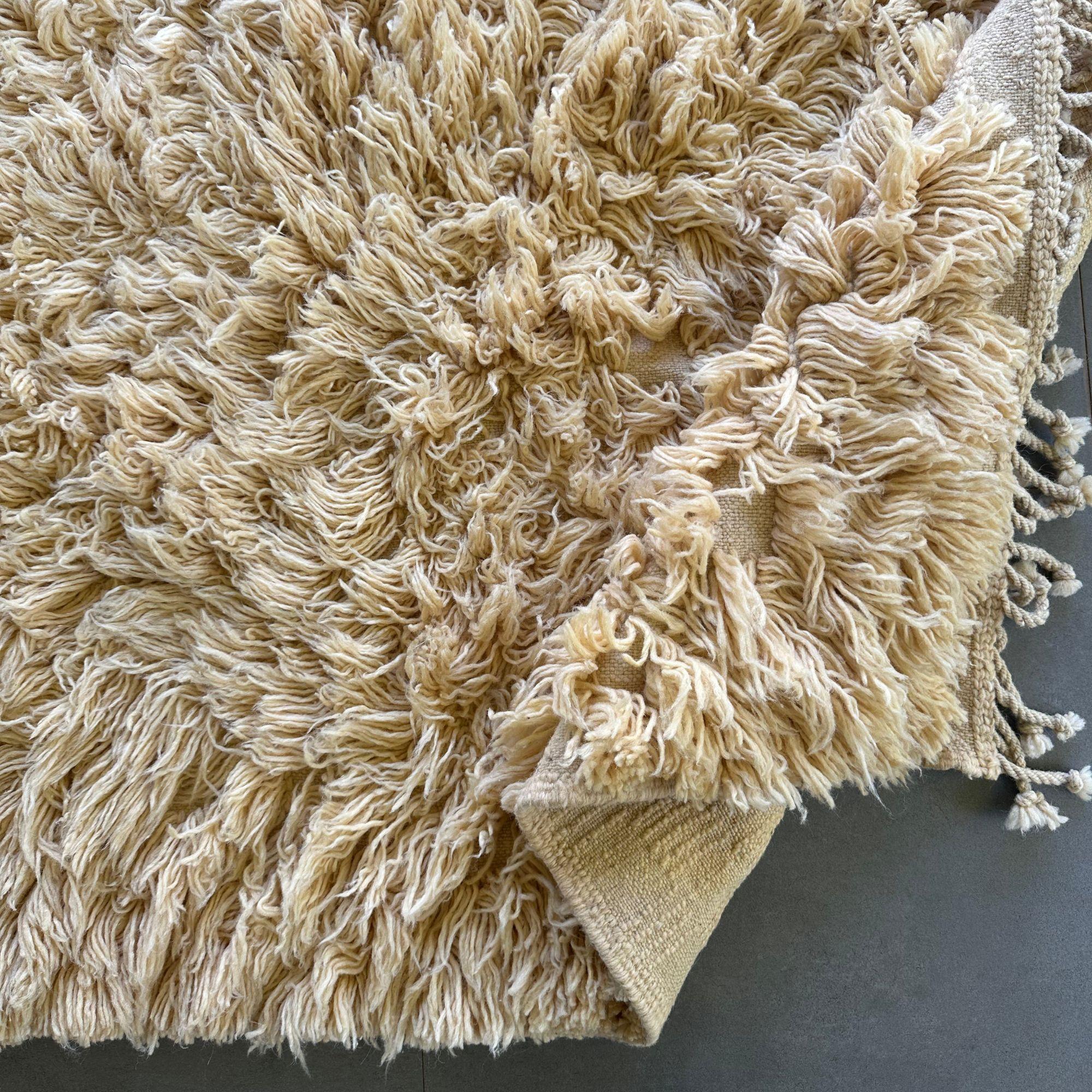 Presentamos el Encanto Celestial, una lujosa alfombra marroquí de pelo alto que aporta un elemento de elegancia y confort a cualquier espacio. Esta exquisita alfombra de color crema presenta un pelo alto afelpado, que ofrece una textura suave y