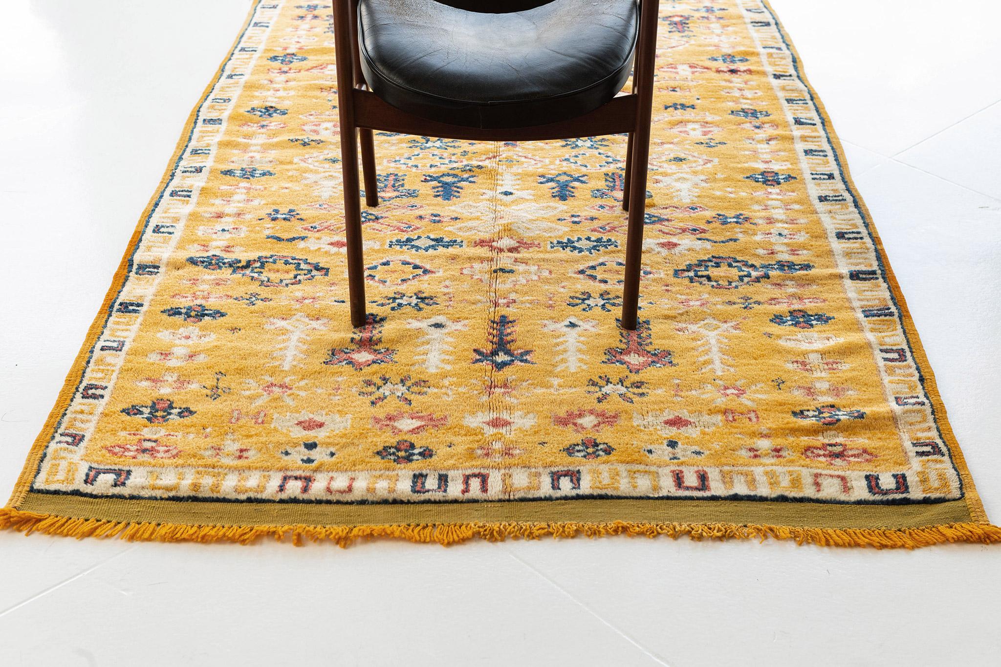 A captivating Vintage Moroccan rug in High Atlas Tribe Collection that features a variety of elaborate symmetrical motifs all over the golden field emanating its vibrant tribal feel. Moroccan rugs are known for the symbolism that is meticulously