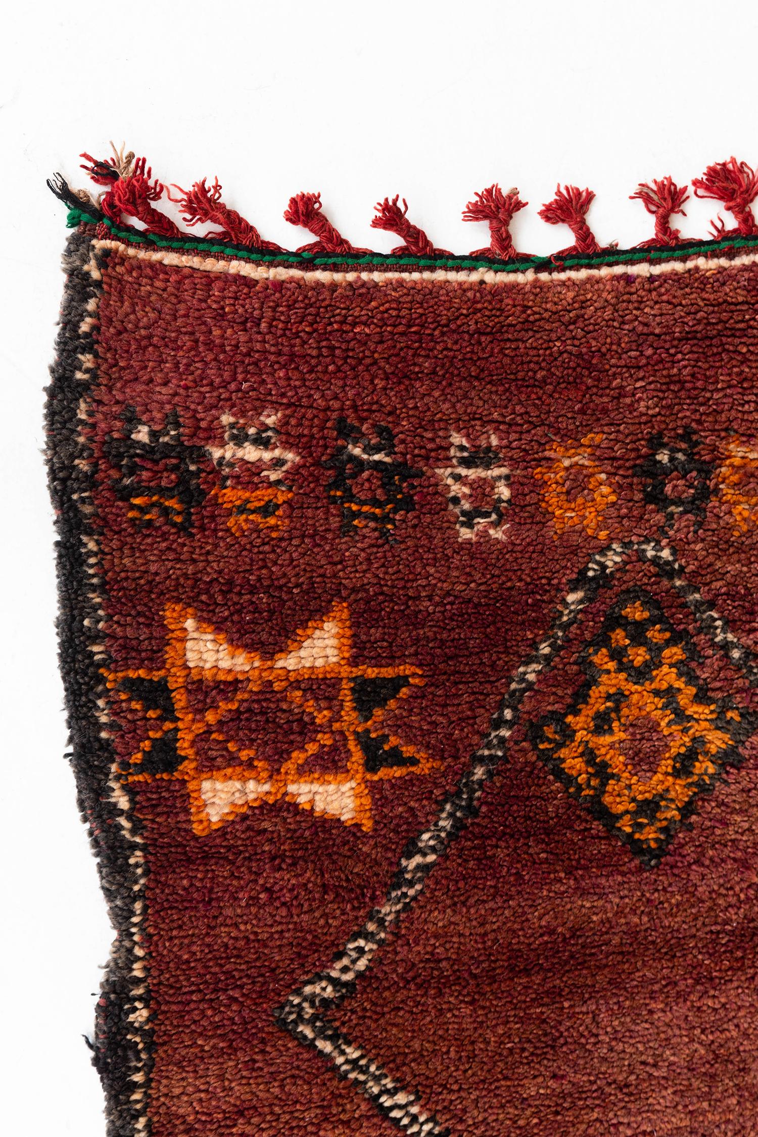 Ein prächtiger marokkanischer Teppich aus unserer Atlas-Kollektion mit einer Reihe von Kreuzformen, die zu einem geometrischen Muster zusammengefügt sind, das auch Rauten enthält. Ein rotes Ziegelholz zeigt Sterne, Fischskelette und einige