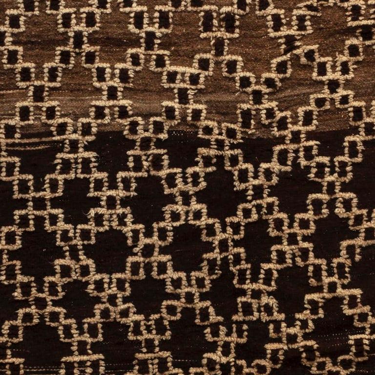 Un motif de treillis crème sur un fond brun chocolat, avec une petite section de gris. Les glands d'origine se trouvent à l'une des extrémités, comme prévu.
Tissé en poils de mouton et de chèvre. Ourika, années 1950
Mesures : 135 x 284cm.


