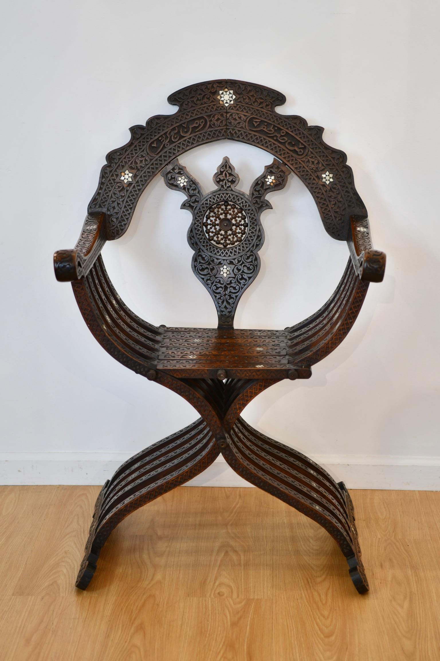 Moroccan carved and shell-inlaid folding Savonarola armchair with scrolling borders, mother of pearl star motifs, and Arabic inscription “من صبر ظفر ومن لج كفر”. Dimensions: 40.5