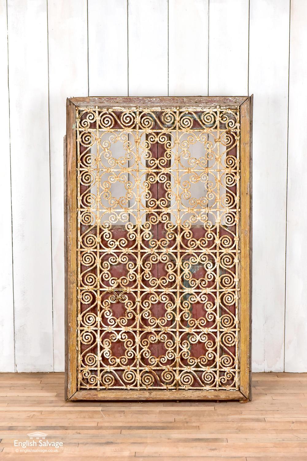 Moroccan shutters and ornate iron window grill in frame. The deep red paint is weathered and peeling to reveal old layers of paint, giving an appealing patina. Overall dimensions of the frame are given below, and the doors measure 88cm wide x