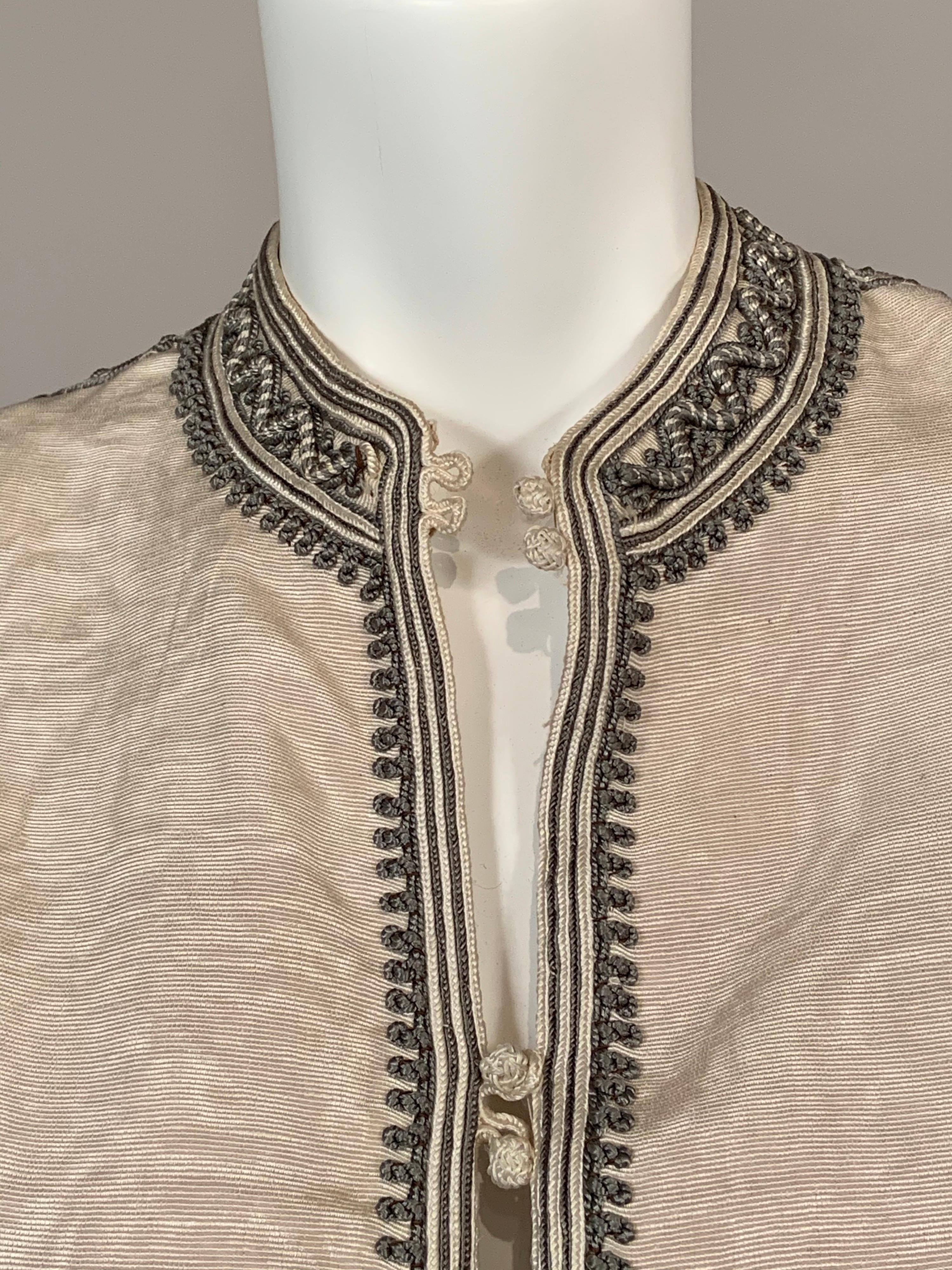 Cream silk faille is lavishly embellished with charcoal grey and cream soutache braid. The collar, front opening, shoulders, sleeves, pockets and cuffs are all decorated with hand applied trim. There are eight buttons and loops at the center front,