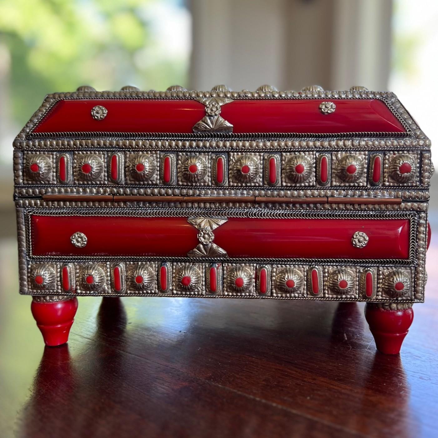 Eine außergewöhnliche marokkanische Schmuck- oder Andenkenschatulle aus dem frühen 20. Jahrhundert, reich verziert mit einer auffälligen Kombination aus versilbertem Metall und tiefroten Bakelitplatten. Diese opulente Schatulle steht auf