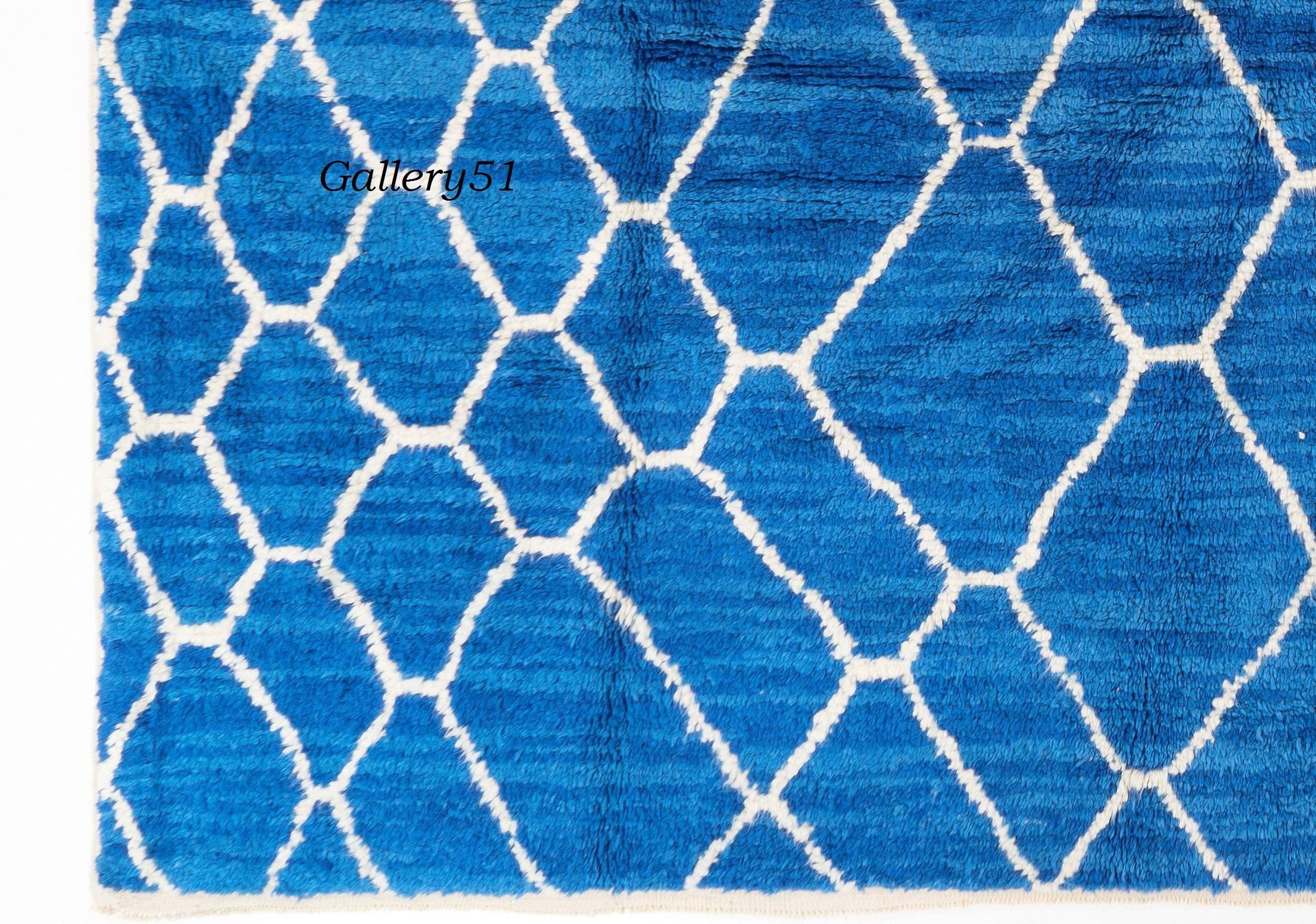 The slightly darker and lighter hues of the striated indigo blue field of this eye-catching Moroccan design contemporary hand knotted rug makes it look as if it's shimmering deep inside.
With a white net of loosely shaped lozenges of differing scale