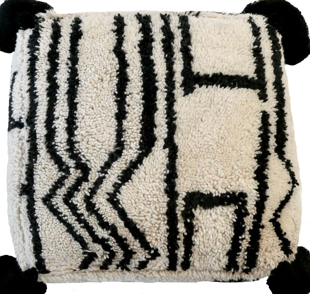 Marokkanischer Hocker aus einem abstrakten Teppich aus der Mitte des Jahrhunderts, handgewebt aus elfenbeinfarbener und schwarzer Wolle. Handgefertigte Quastenakzente und ein Kelim auf der Rückseite. Neuer maßgeschneiderter Dauneneinsatz mit