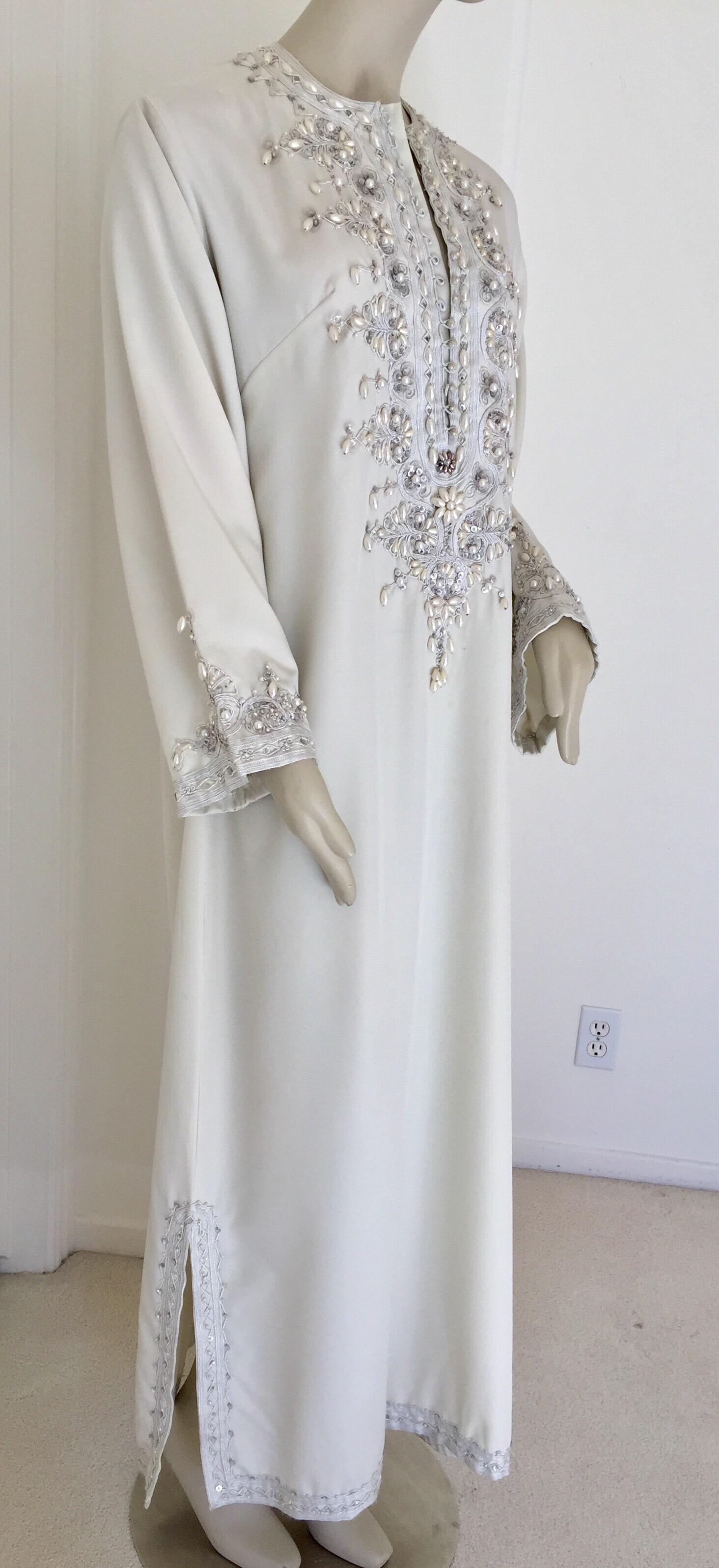Moroccan caftan, evening or interior adorned with white pearls.
Handcrafted vintage exotic 1970s kaftan gown.
The luminous white poly jersey maxi dress caftan is adorned in front with metallic floral embroidered patterned and white pearls and silver