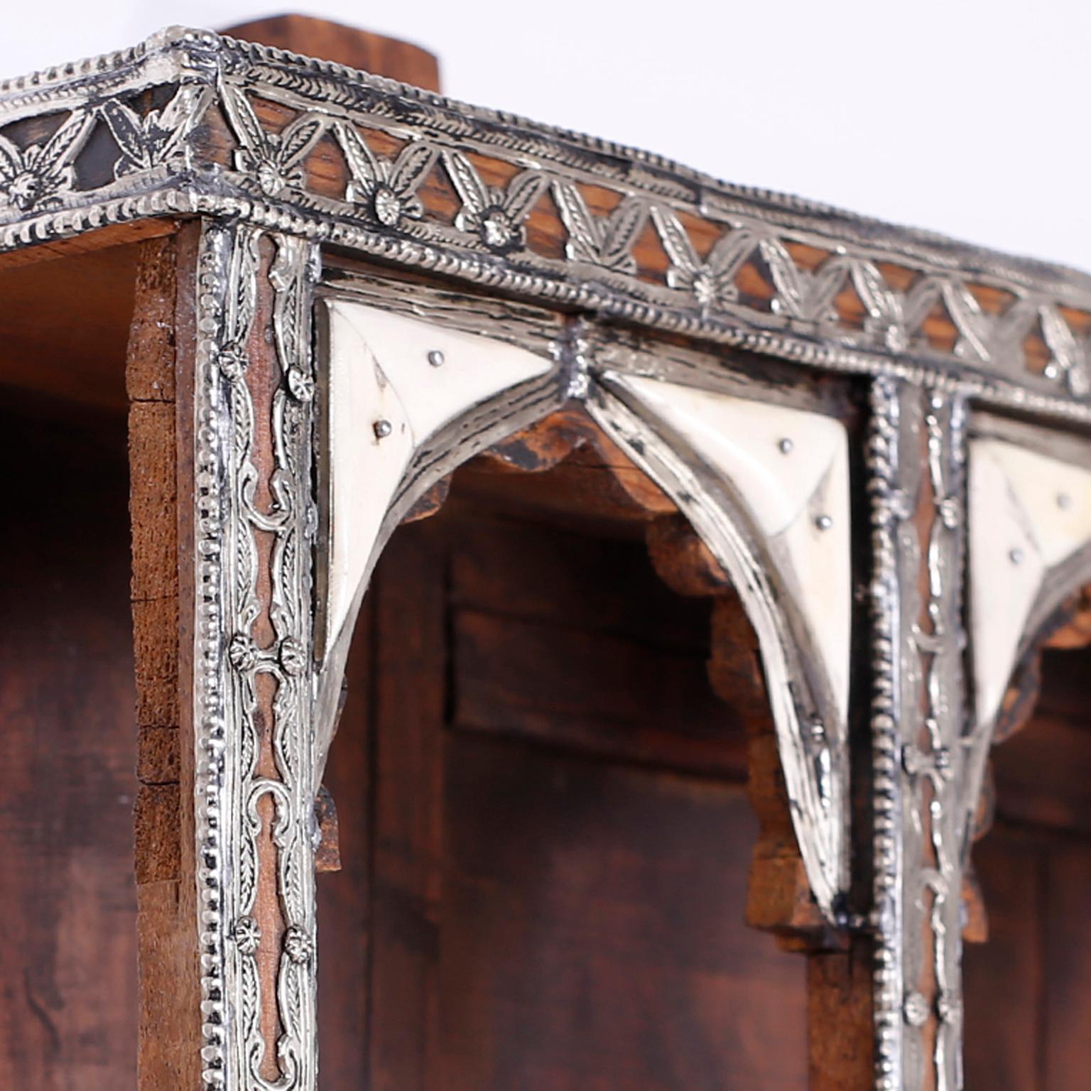 Antique Moroccan wall display shelf with a charming rustic ambiance crafted in mahogany with architectural Moorish arches and nooks. Featuring hand-hammered geometric and floral applied silvered metal designs and highlighted with bone.