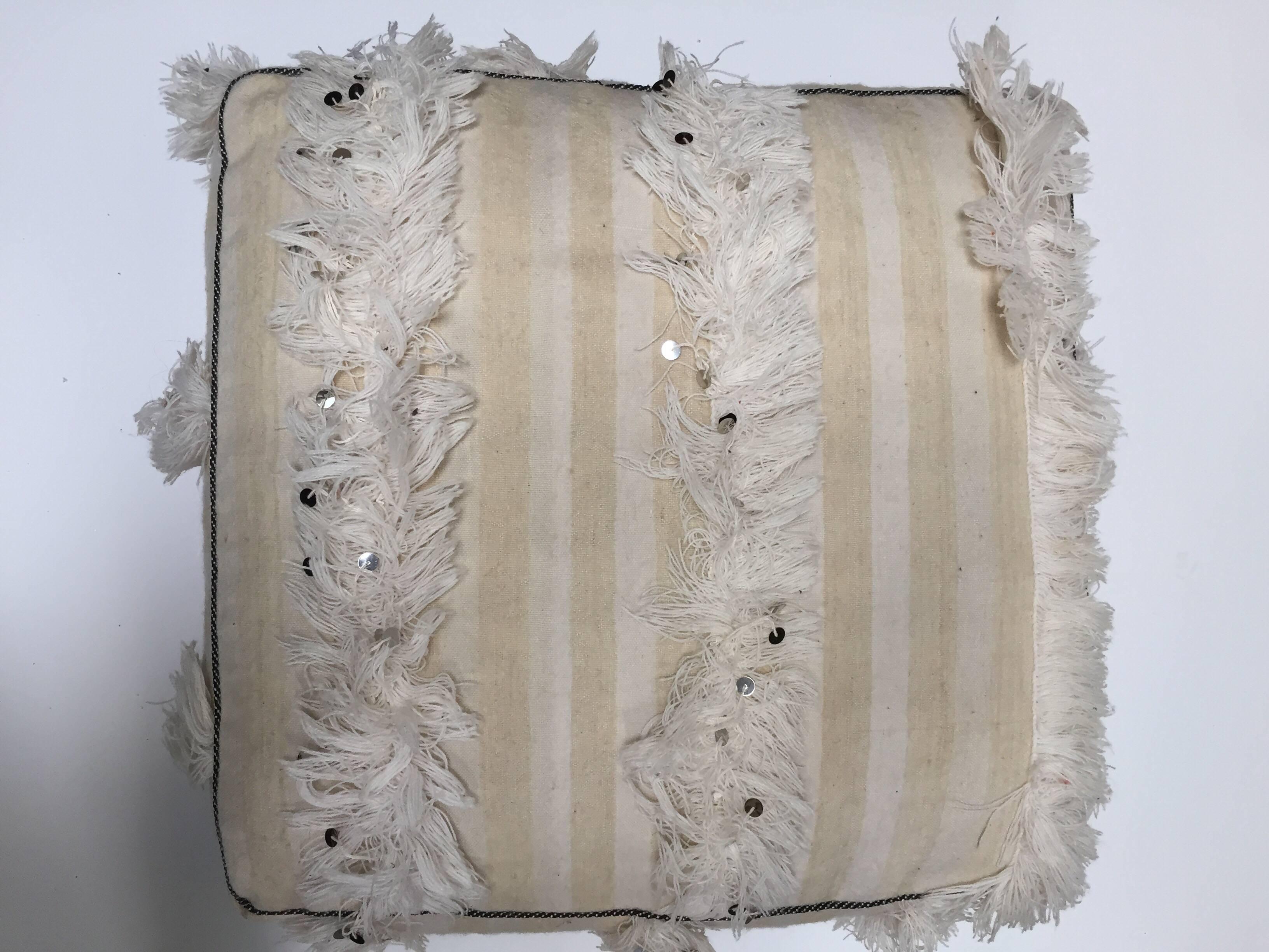 This handcrafted vintage Moroccan tribal floor pillow or pouf is made from a traditional handwoven white wool and cotton throw used by the Berber women in Morocco for their wedding.
Handmade wool Berber wedding blanket with silver sequins and long