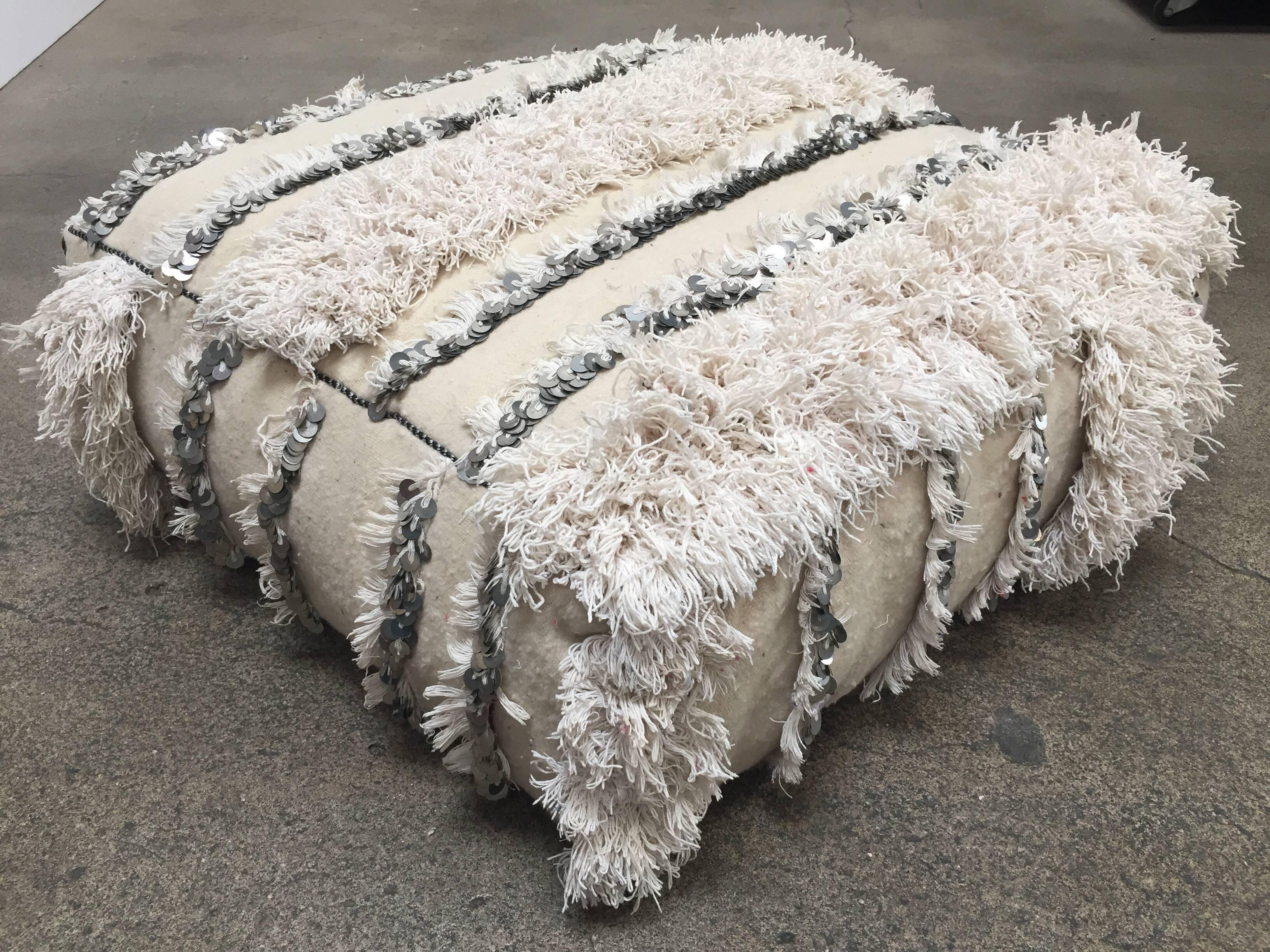 This handcrafted vintage Moroccan tribal floor pillow or pouf is made from a traditional handwoven white wool and cotton throw used by the Berber women in Morocco for their wedding.
Handmade wool Berber wedding blanket with silver sequins and long