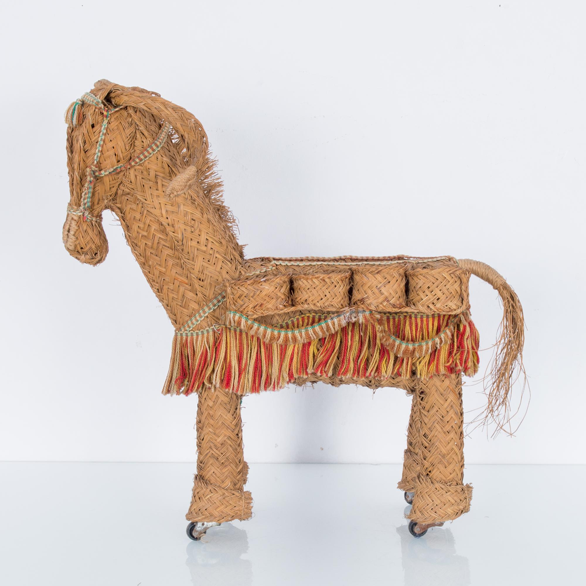 A decorative wicker donkey on wheels from Morocco, circa 1960s. An artisan piece with a rustic, Mediterranean feel. Wicker side baskets evoke goods sold at a market or roadside, while decorative fringe adds a carnival touch of color. The jaunty tilt