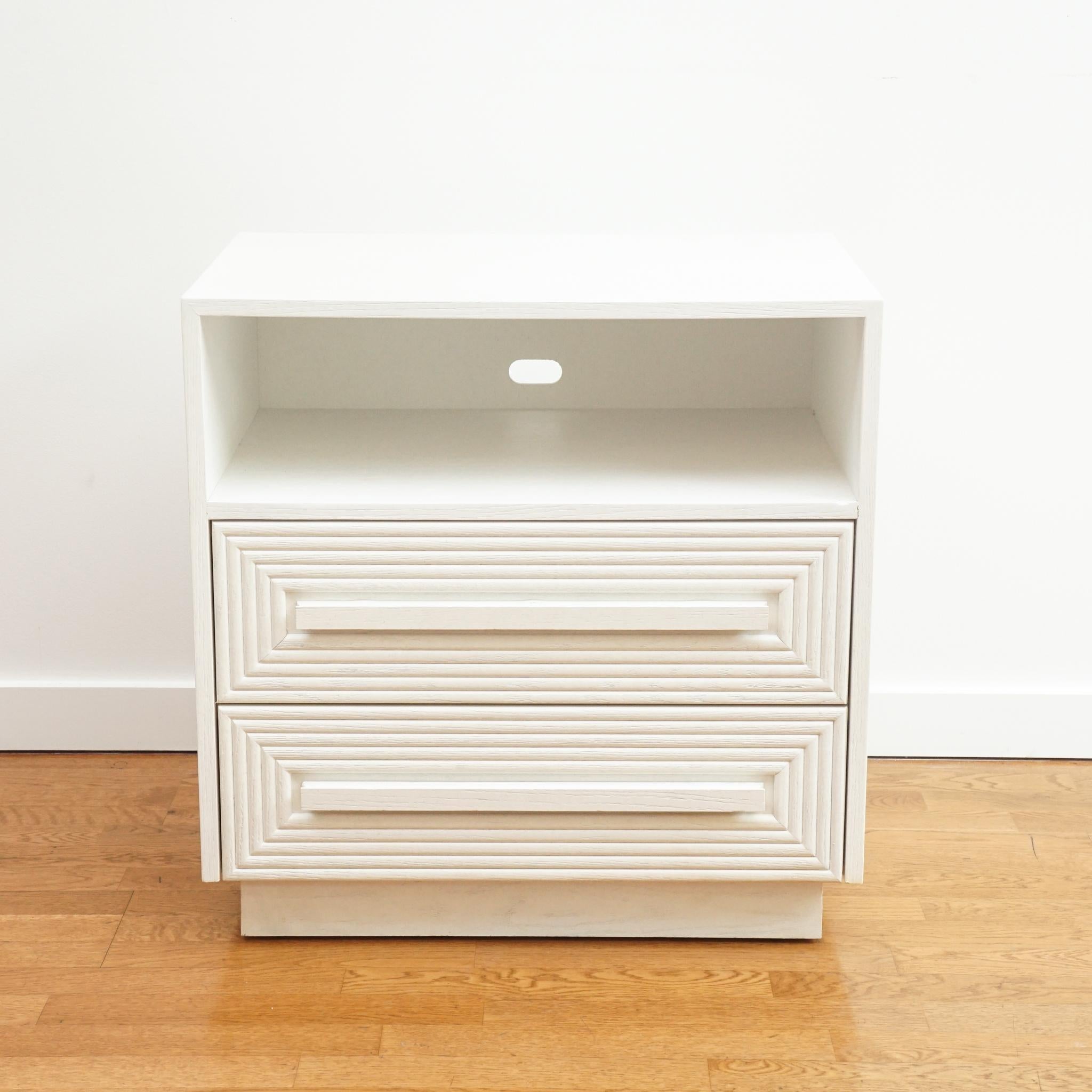 The Morombe white cerused nightstand, shown here, is as notable for its design as its finish. Made of white oak, the drawer fronts feature a rectangular carved design that is accentuated by a long horizontal wood pull.  The white cerused finish is a