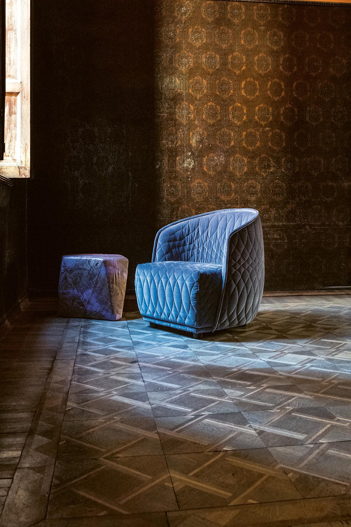 An armchair with a distinctive two–part shape, the padded shell embraces the huge seat cushions. Its curves are shown off by the total absence of sharp corners and the softness of the fabric, and the quilted decoration where the thread, like the