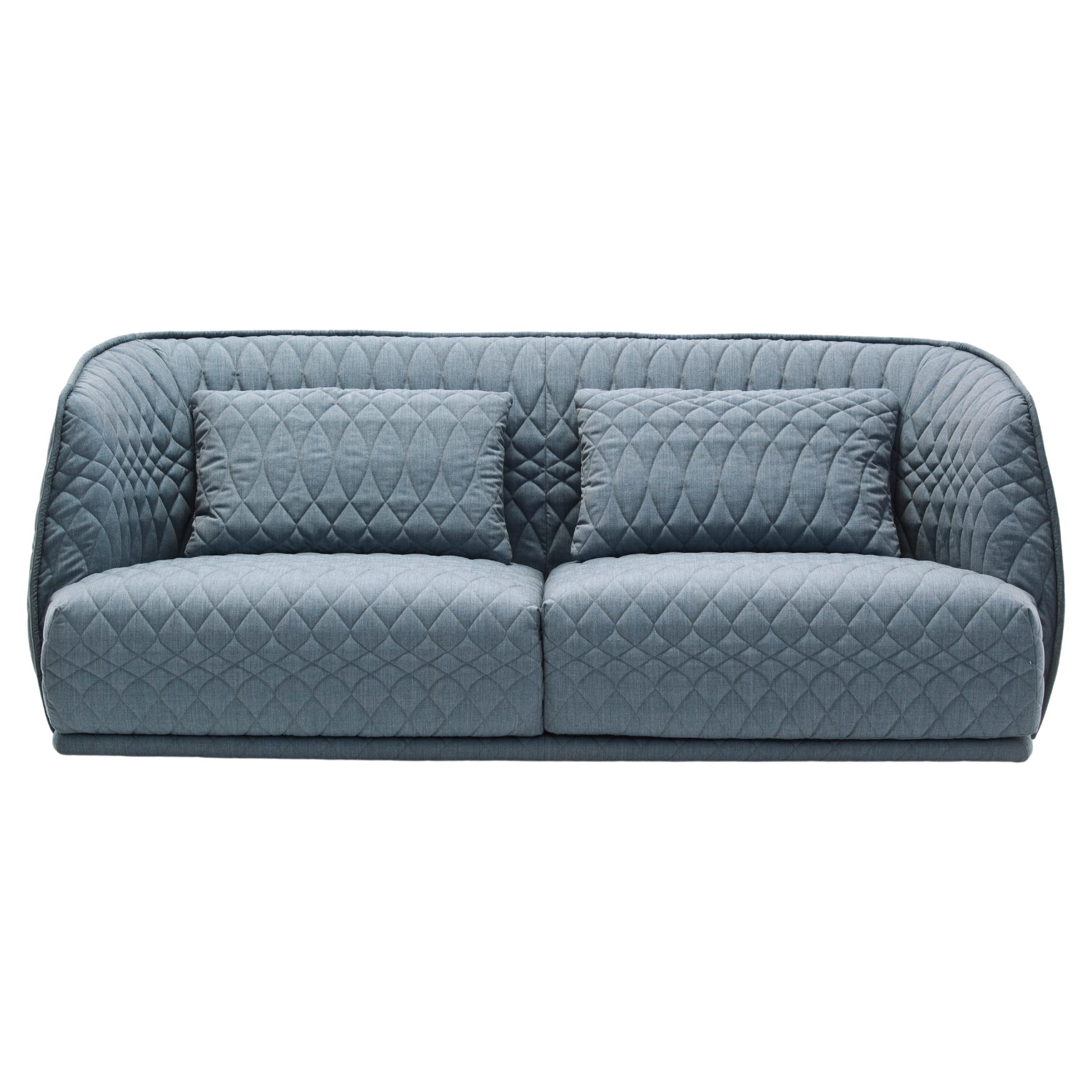 A collection with a distinctive two–part shape, the padded shell embraces the huge seat cushions. Its curves are shown off by the total absence of sharp corners and the softness of the fabric, and the quilted decoration where the thread, like the