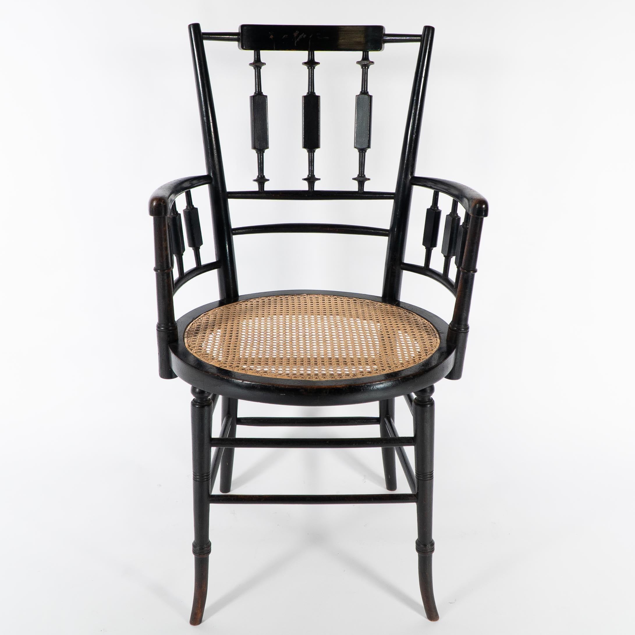 An Aesthetic Movement cane seated armchair by Morris and Co with circular cane seat. A variant is illustrated in the Liberty Yuletide Gifts catalogue.