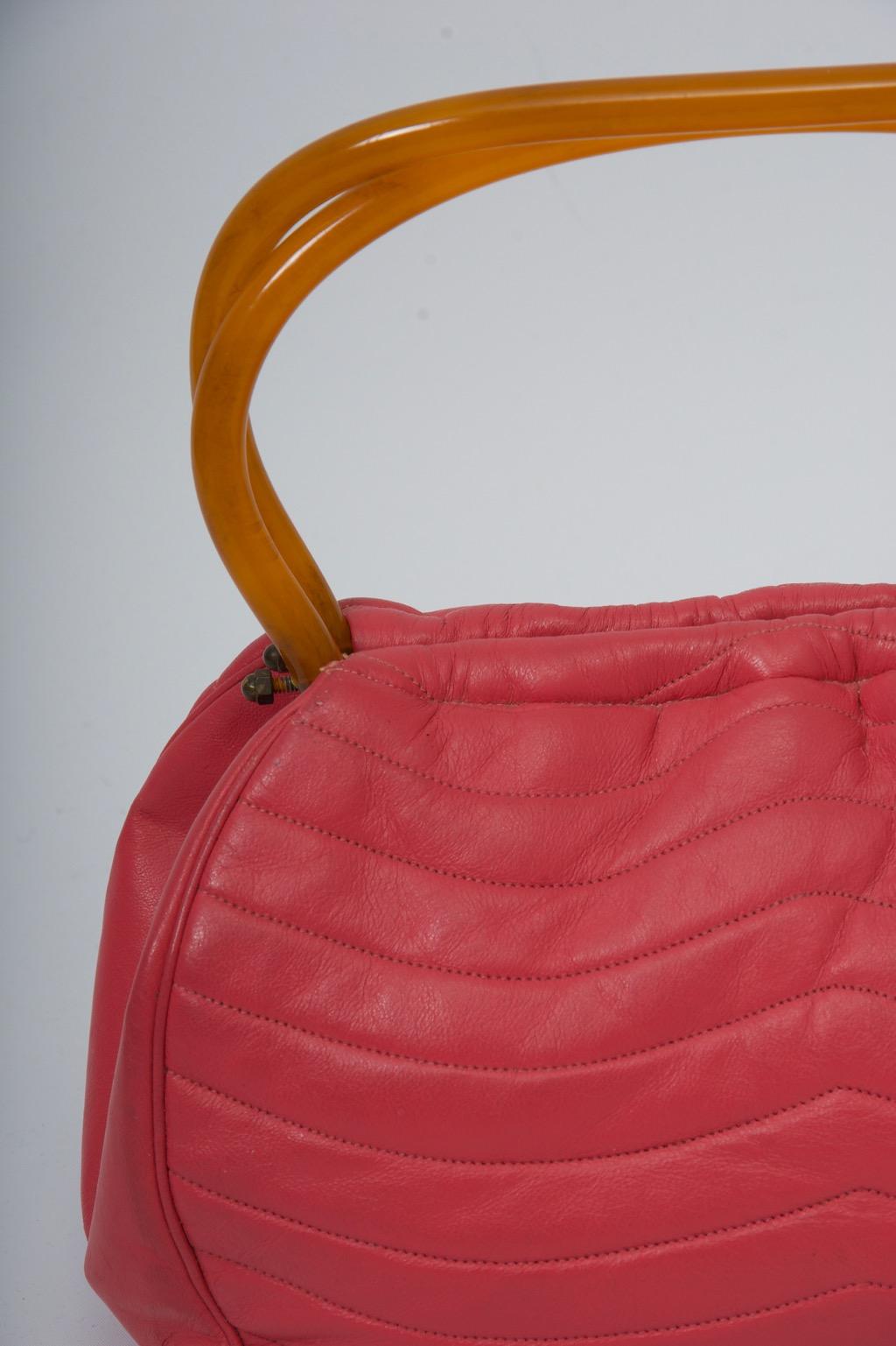 MM handbag c.1960s in dark pink, the leather featuring horizontal, curved stitching resulting in a quilted effect. The faux tortoise handles echo the shape of the bag and snap together to close. A coordinating faille interior has an attached money