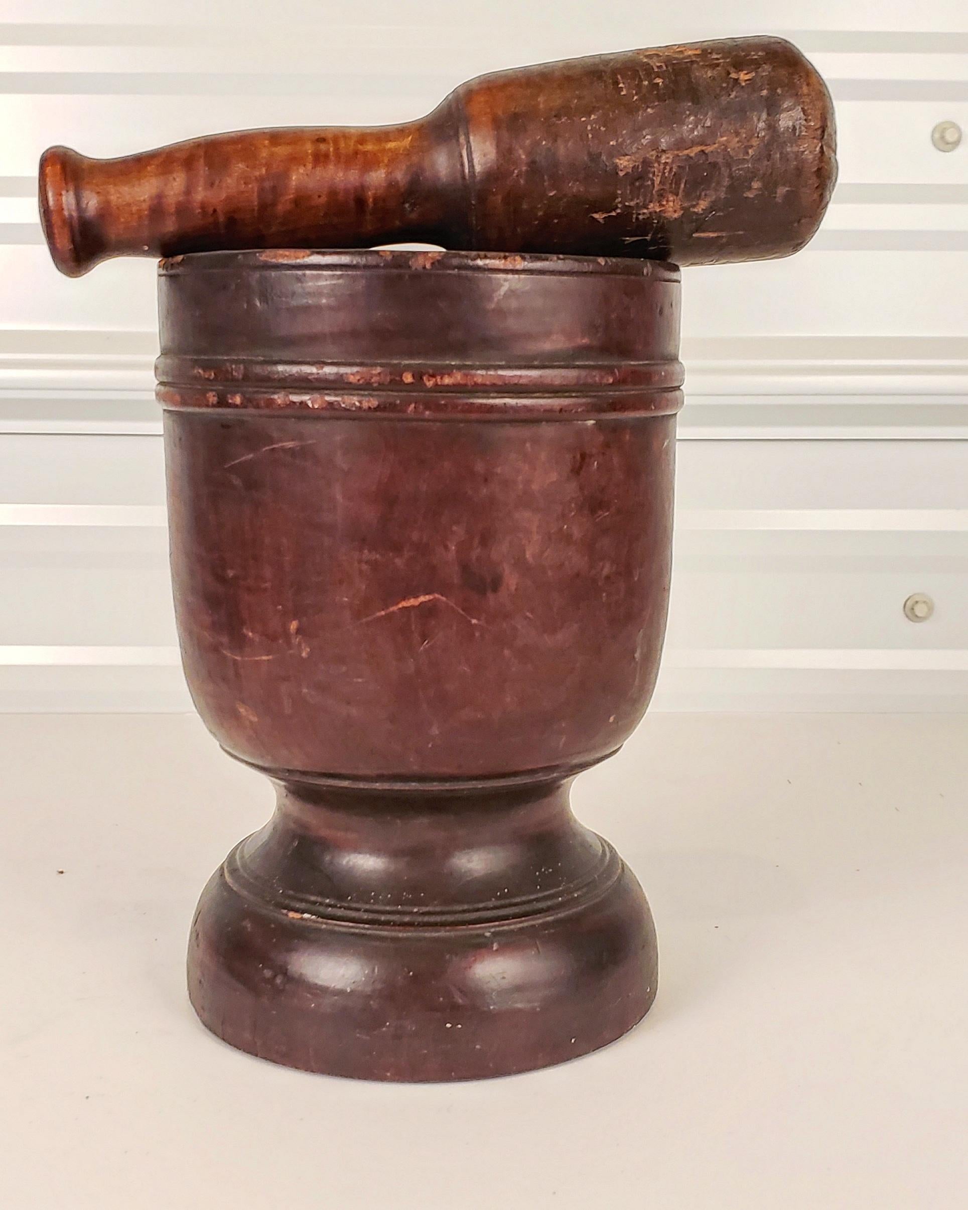 Amerikanischer, hölzerner Mörser und Stößel aus dem späten 18. und frühen 19. Jahrhundert. Der urnenförmige Mörser mit reicher Patina hat eine wunderbare Wärme und Haptik. Der Sockel ist ergonomisch korrekt für das Halten mit der Hand.
Der Stößel