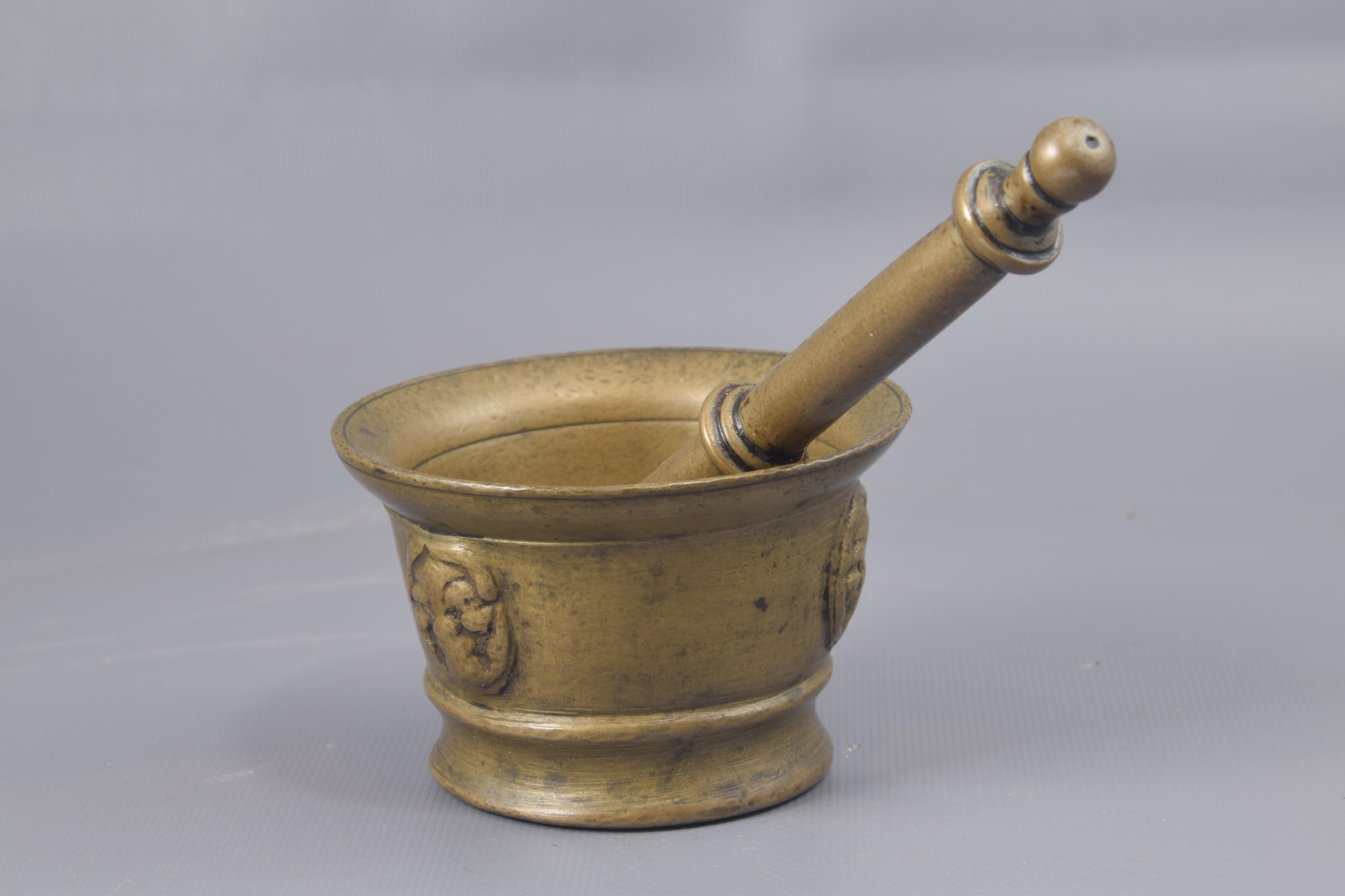 Mortar with mace. Bronze. XVII century. 
Bronze mortar with a cylindrical body that shows the excavated mouth (with two fine lines inside), the base with a concave molding and the smooth front decorated with elements in relief reminiscent of masks;