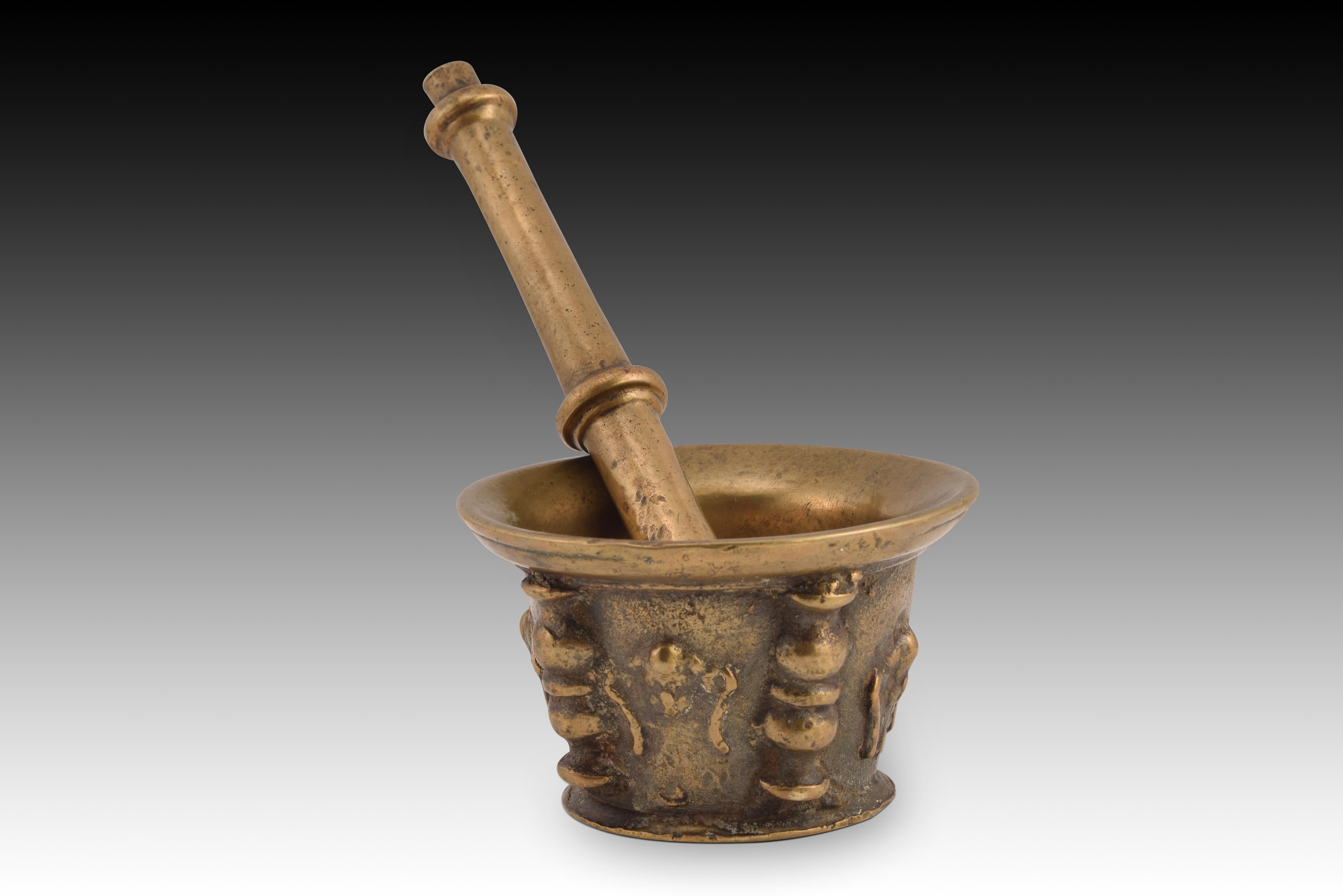 Mortar with pestle. Bronze. Spanish school, 17th century. 
Bronze mortar with a convex mouth, a raised base facing outwards and a cylindrical body decorated on the outside with reliefs alternating shapes (probably figurative in origin, perhaps angel