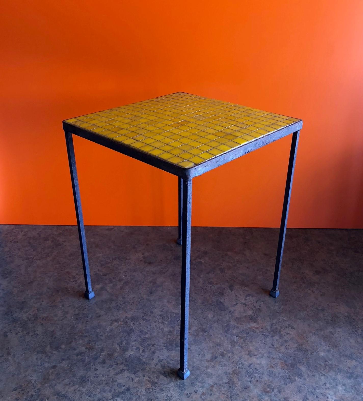 Vibrant yellow mosaic top side table in the style of Paul McCobb, circa 1960s. The table has a black iron base with mosaic glass tile tops in the shade of yellow. Would brighten up any mid-century room or work great on a covered patio!