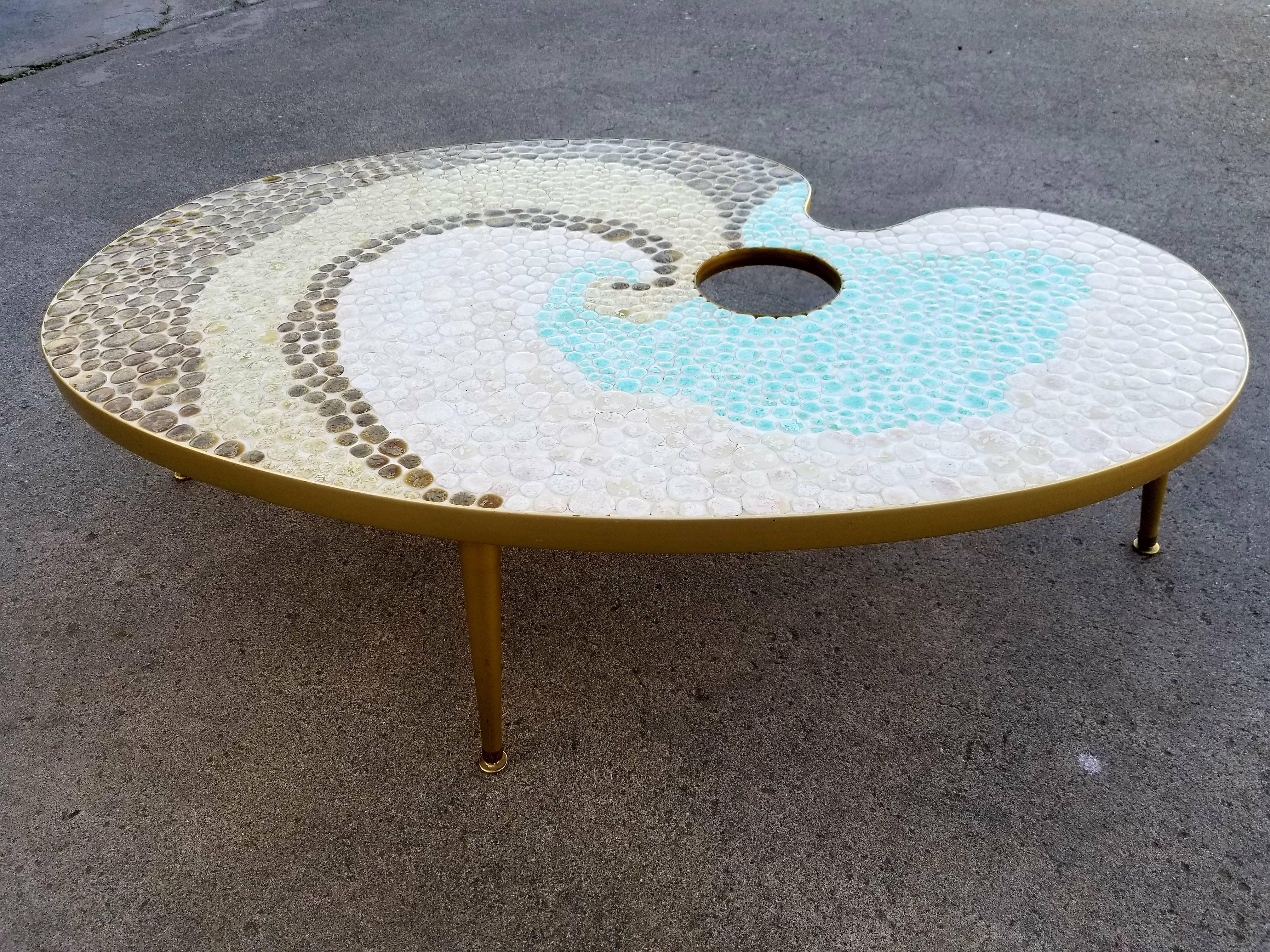 A unique mosaic tile coffee table in the form of an artist’s palette, circa 1950s. Brown, turquoise and off-white circular tiles. Brass apron with brass peg legs.
