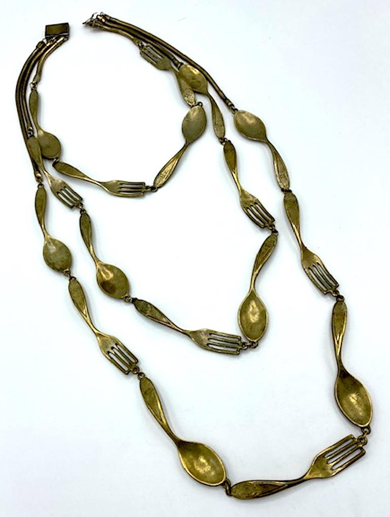 An amazing 1980s necklace from the edgy fashion house of Moschino. There are three stands of alternating 3 inch long curved forks and spoon. Each strand is attached to a snake link chain at the for comfort around the neck. The three snake chains