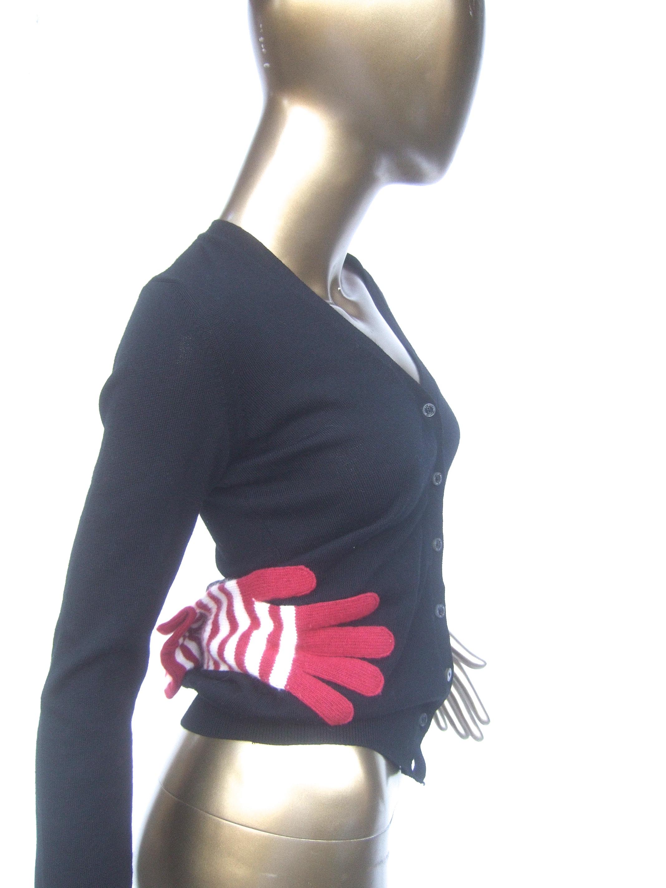 Moschino avant-garde Italian black wool glove design cardigan 
The unique fine wool knit cardigan is designed with a pair of red & white striped wool knit gloves sewn on each of the sides of the cardigan 

The lower back section is designed with a