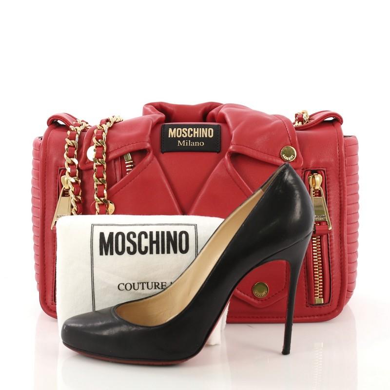 This Moschino Biker Bag Leather Medium, crafted from red leather, features woven-in leather chain strap, exterior zip pockets, and gold-tone hardware. Its flap opens to a black fabric interior with zip and slip pockets. **Note: Shoe photographed is