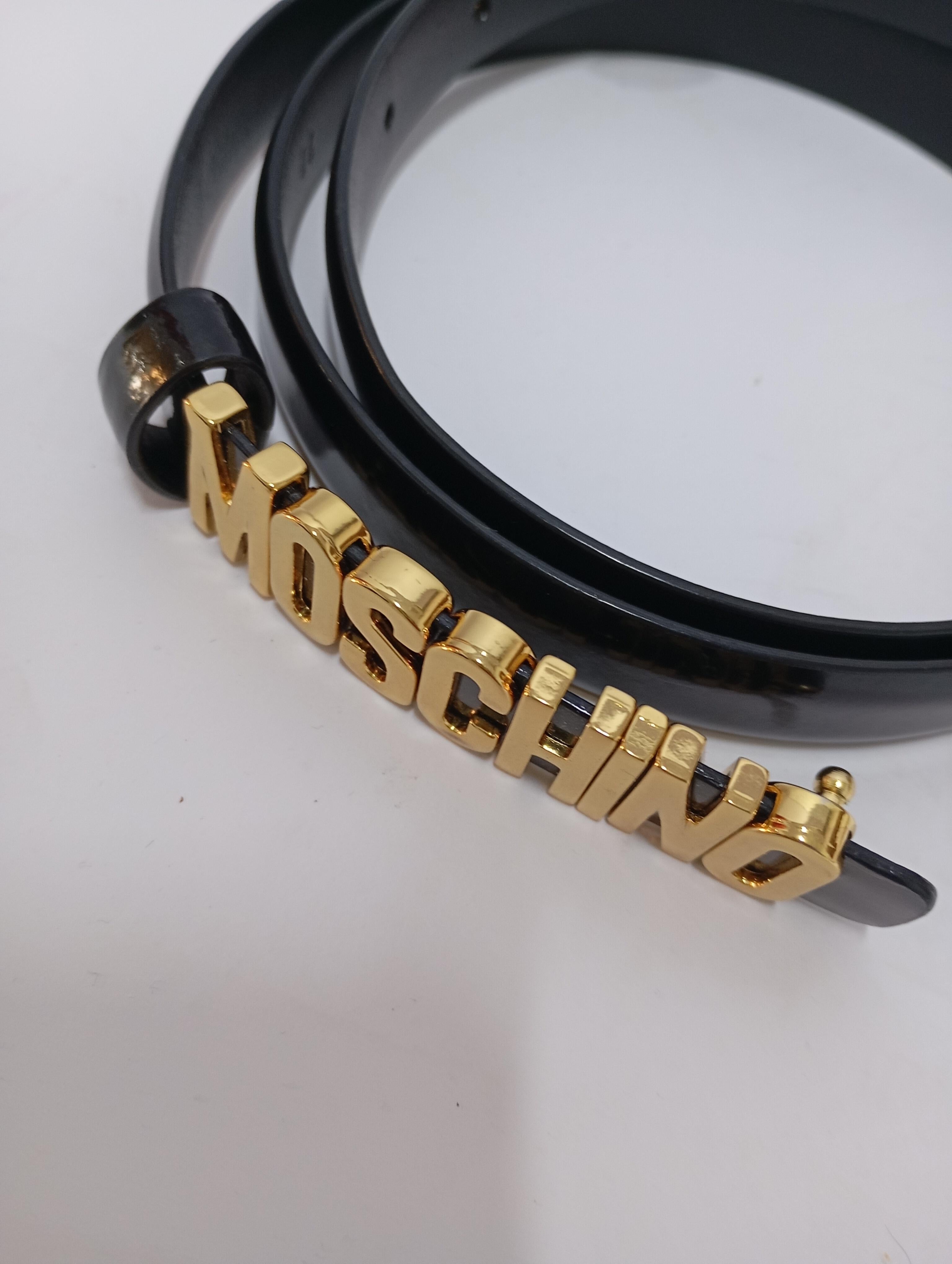Añade un atrevido toque italiano a tu look con este cinturón pitillo de charol negro Moschino, con el logotipo dorado característico de la marca. Elegante y minimalista, con un toque llamativo, este versátil accesorio ciñe perfectamente la cintura