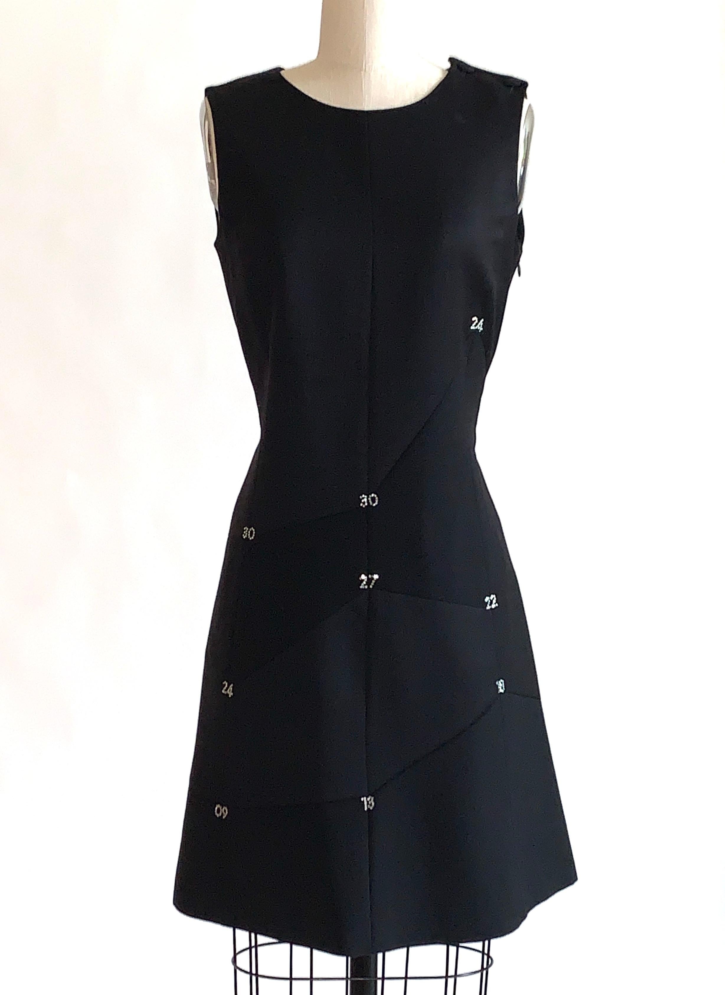 1990s Moschino Cheap & Chic black sleeveless dress with flared skirt. Pieced together with seams connect rhinestone numbers at various points throughout. Two cloth covered buttons at wearer's left shoulder. Side zip. 

100% wool.
Fully lined in 60%