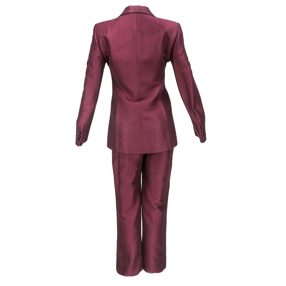 Un abito da smoking chic e tagliato di Moschino. In misto lana e acetato in un bordeaux intenso leggermente cangiante con finiture in lurex nero. Con due bottoni e completamente foderato. Giacca aderente e pantaloni a vita alta. Finte tasche a