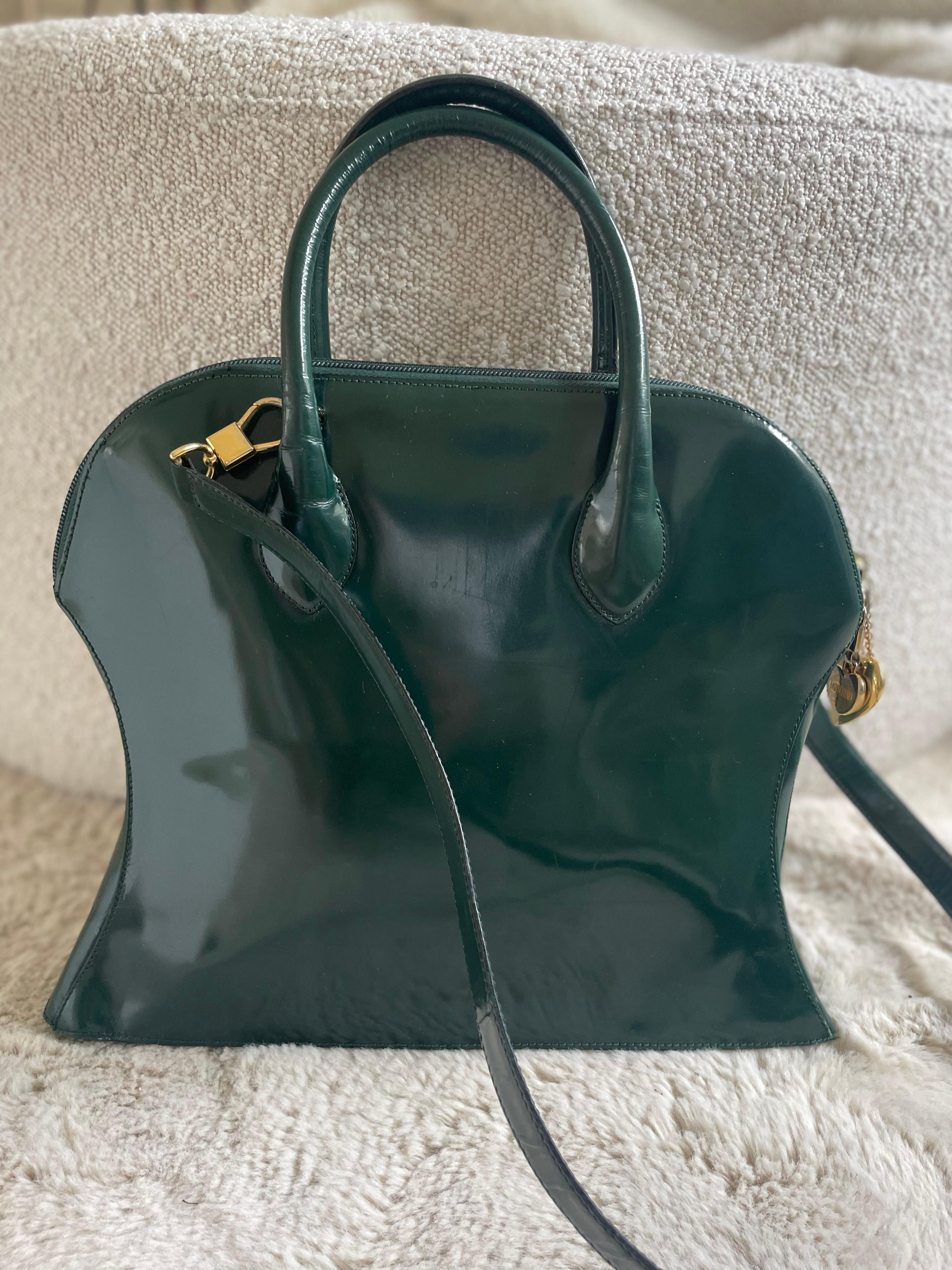Sac à bandoulière vintage Moschino by Redwall en laque verte avec une breloque en forme de cœur en or et une breloque au niveau de la fermeture éclair,  est un mélange parfait de design ludique et de luxe. Sa couleur vibrante, sa texture unique et