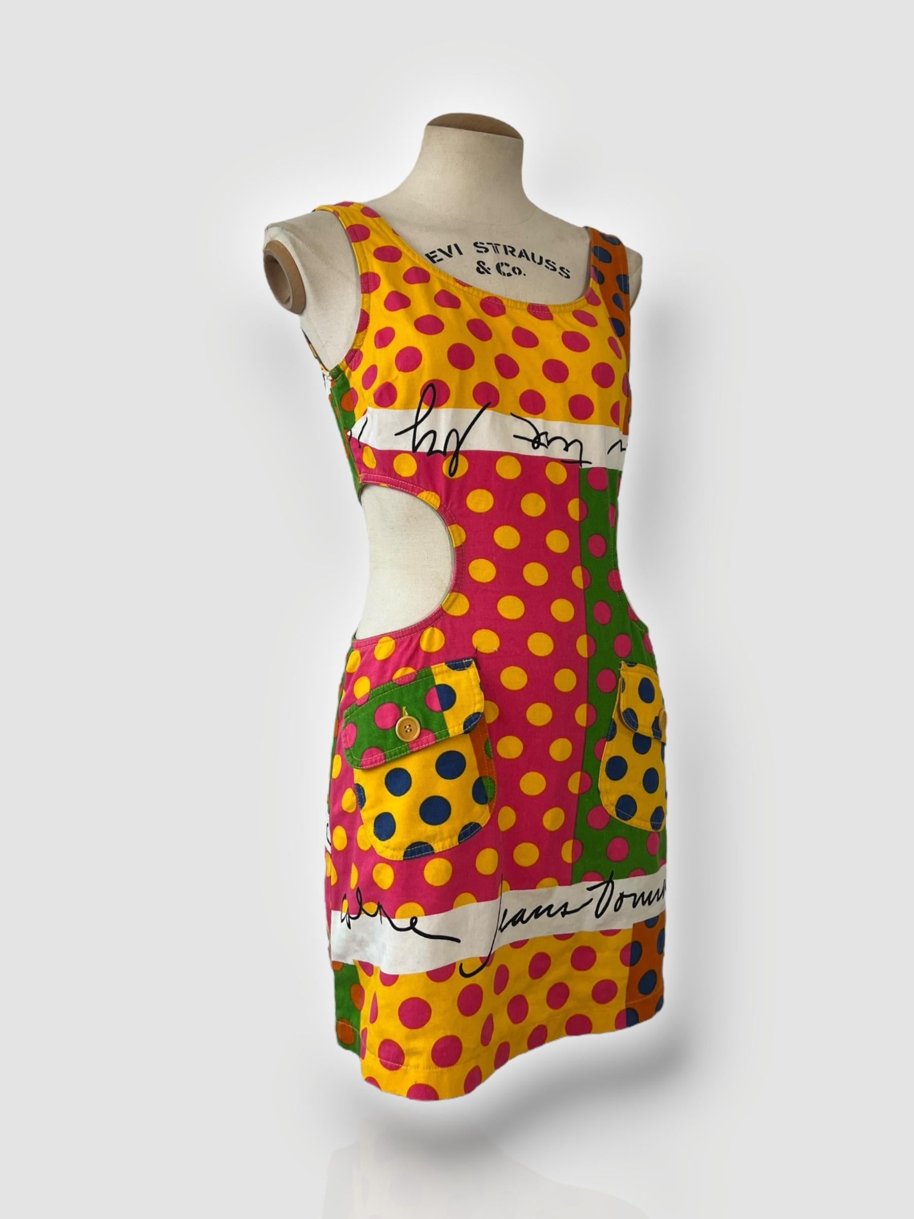 

Un mini abito audace e giocoso di Moschino Cheap and Chic, caratterizzato da una vivace stampa a pois multicolore con i caratteristici dettagli delle scritte. La silhouette d'ispirazione rétro comprende vistosi tagli laterali, due tasche anteriori