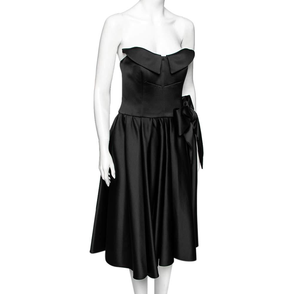 How pretty and feminine is this dress from the House of Moschino Couture! Draped elegantly using black satin fabric, this dress is accentuated with pleated formations and a bow motif on the front. It is equipped with a zip-type fastening. Wear this