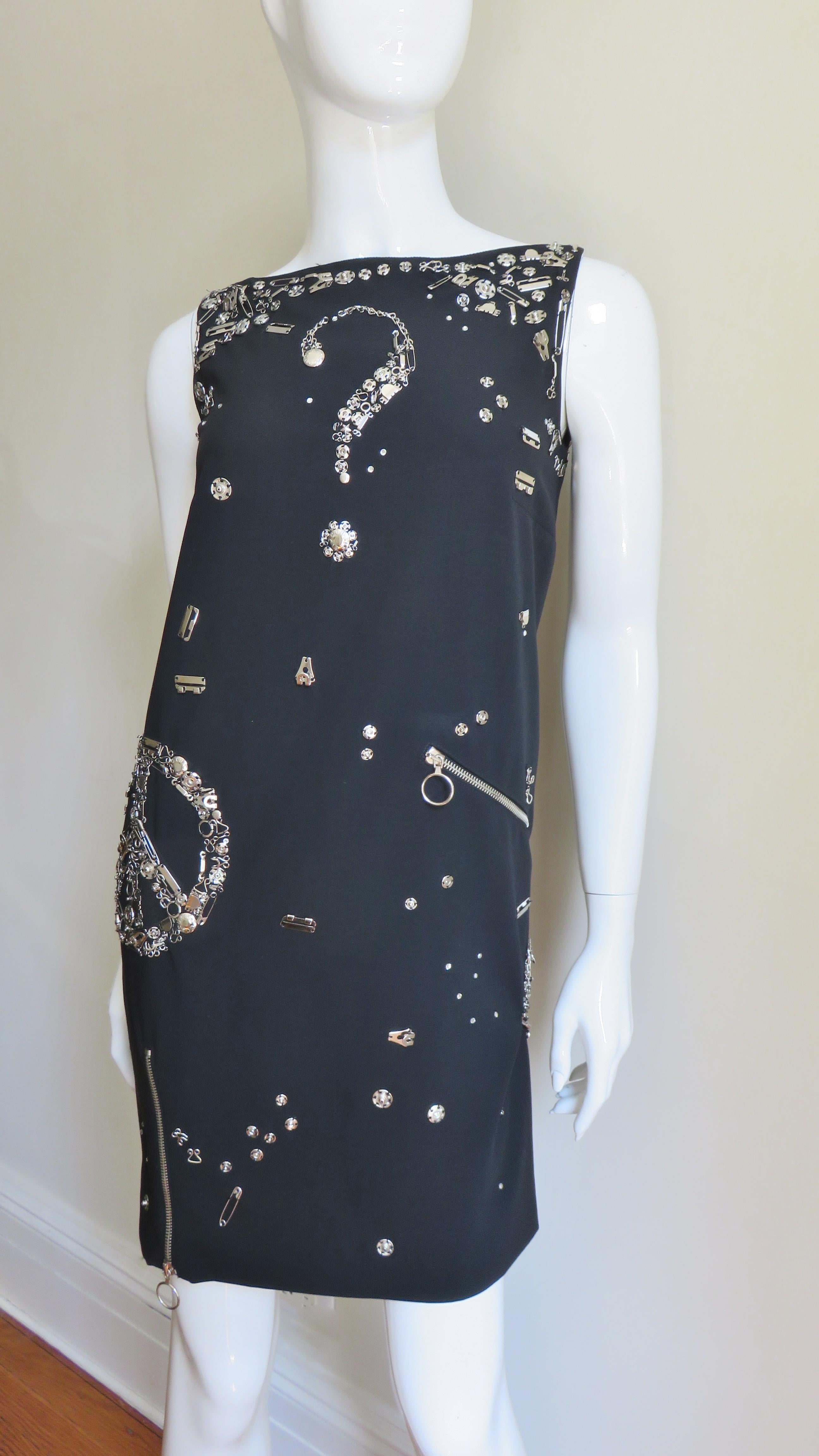 Un favoloso abito nero in lana leggera di Moschino Couture impreziosito da minuteria metallica argentata di vario tipo.  Si tratta di un abito senza maniche con cerniere funzionali sull'orlo anteriore che si aprono per creare uno spacco, oltre alla