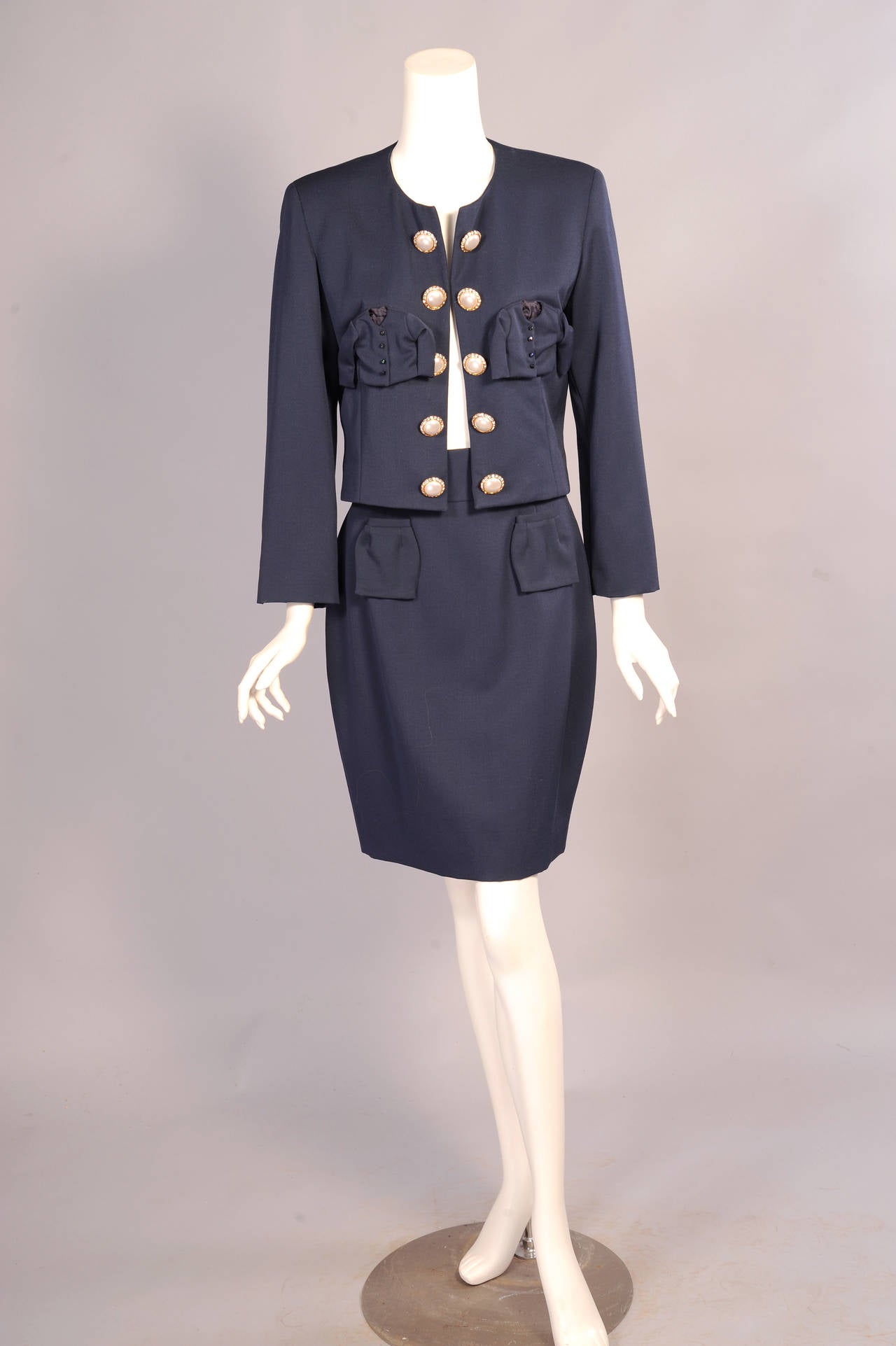 Franco Moschino  ha disegnato questo abito in lana blu navy con l'idea di prendere in giro il classico abito Chanel. An He ha utilizzato una forma simile e bottoni simili. L'umorismo viene dalle tasche. Al posto delle tradizionali tasche della