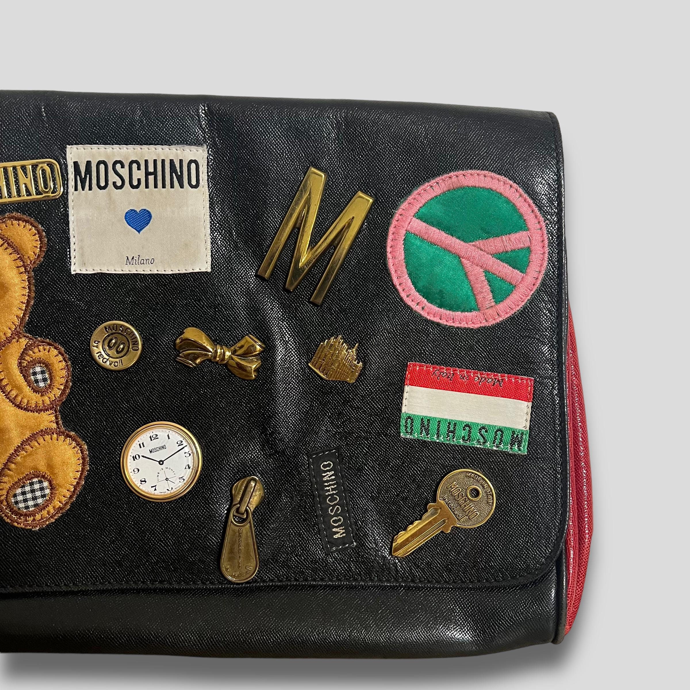 Esta bolsa icónica de la línea Moschino Couture presenta una mezcla ecléctica de apliques de dibujos animados y accesorios caprichosos, como un osito de peluche, un signo de la paz, una llave y un reloj, todos ellos símbolos por excelencia del
